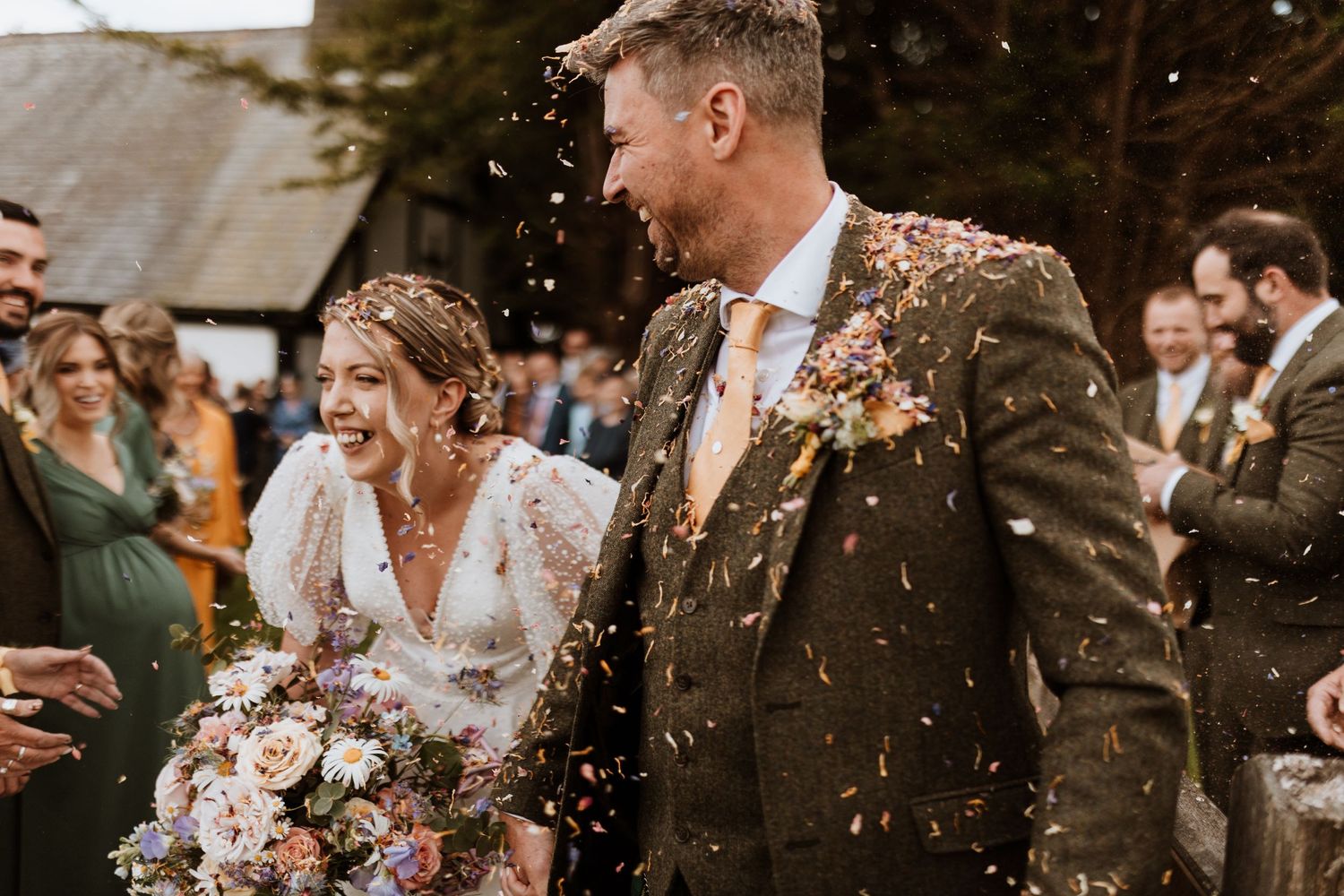 Newlyweds walk through shower of confetti with autumn bouquet and rustic barn backdrop at Quaint Country Weddings