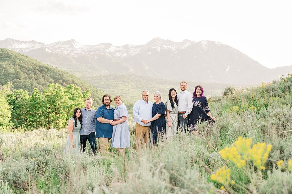 A small group stands together on a hillside with mountains and green foliage in the background.