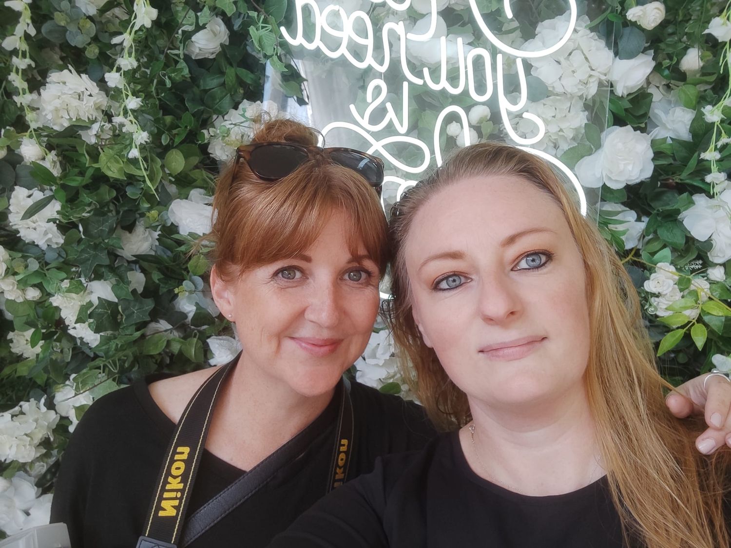 Two photographers stand in front of a floral backdrop with white roses.