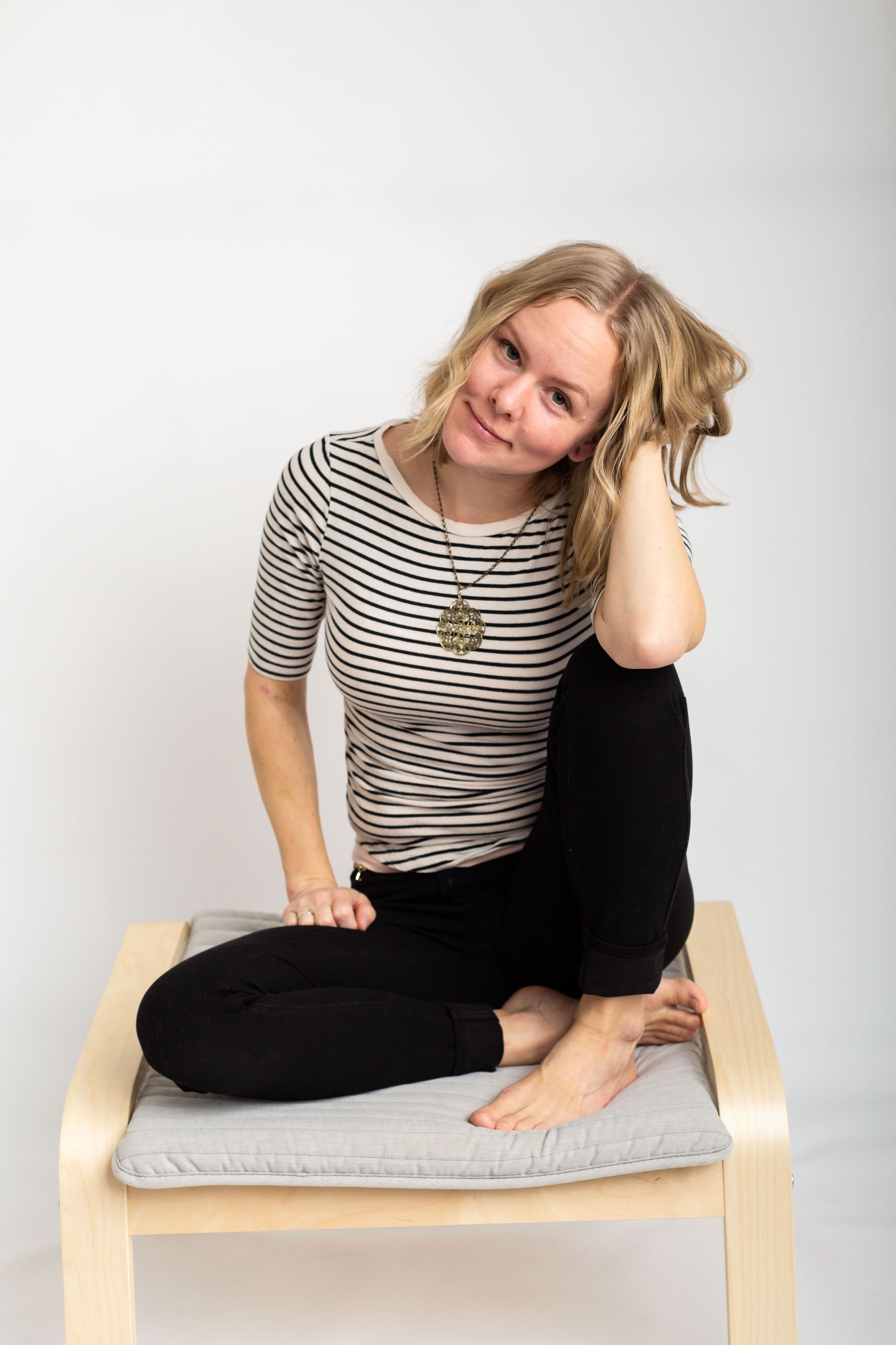 Person in striped shirt sitting casually on a cushioned wooden chair against white background.