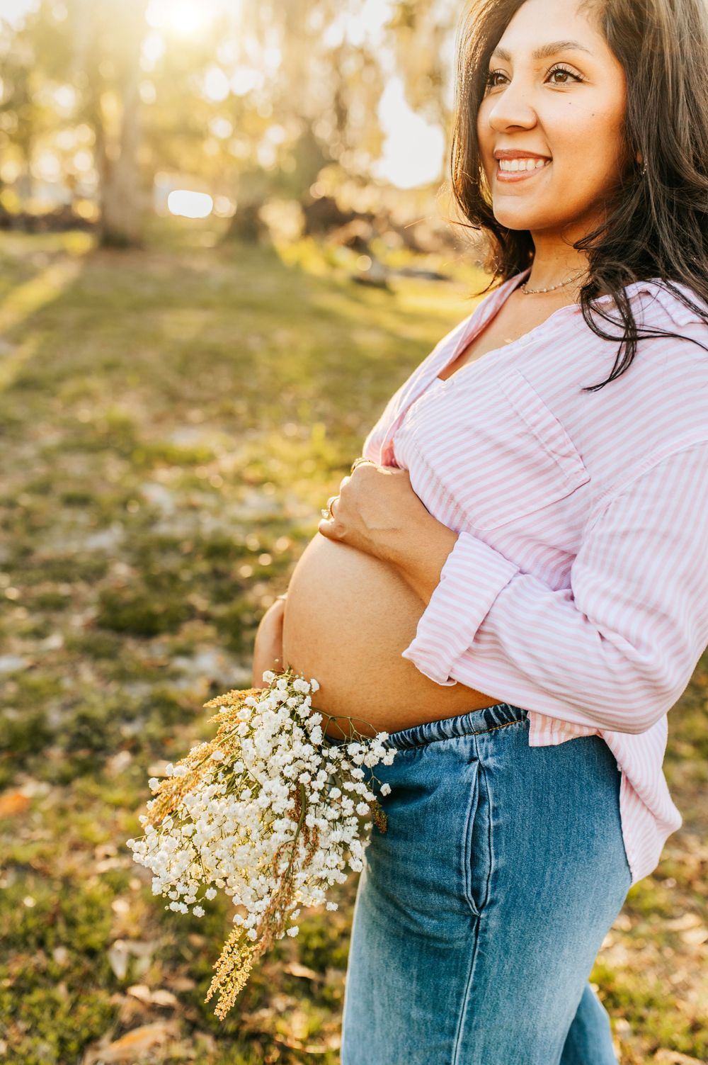 Maternity photos featuring baby's breath flowers and pink striped top against natural backdrop.