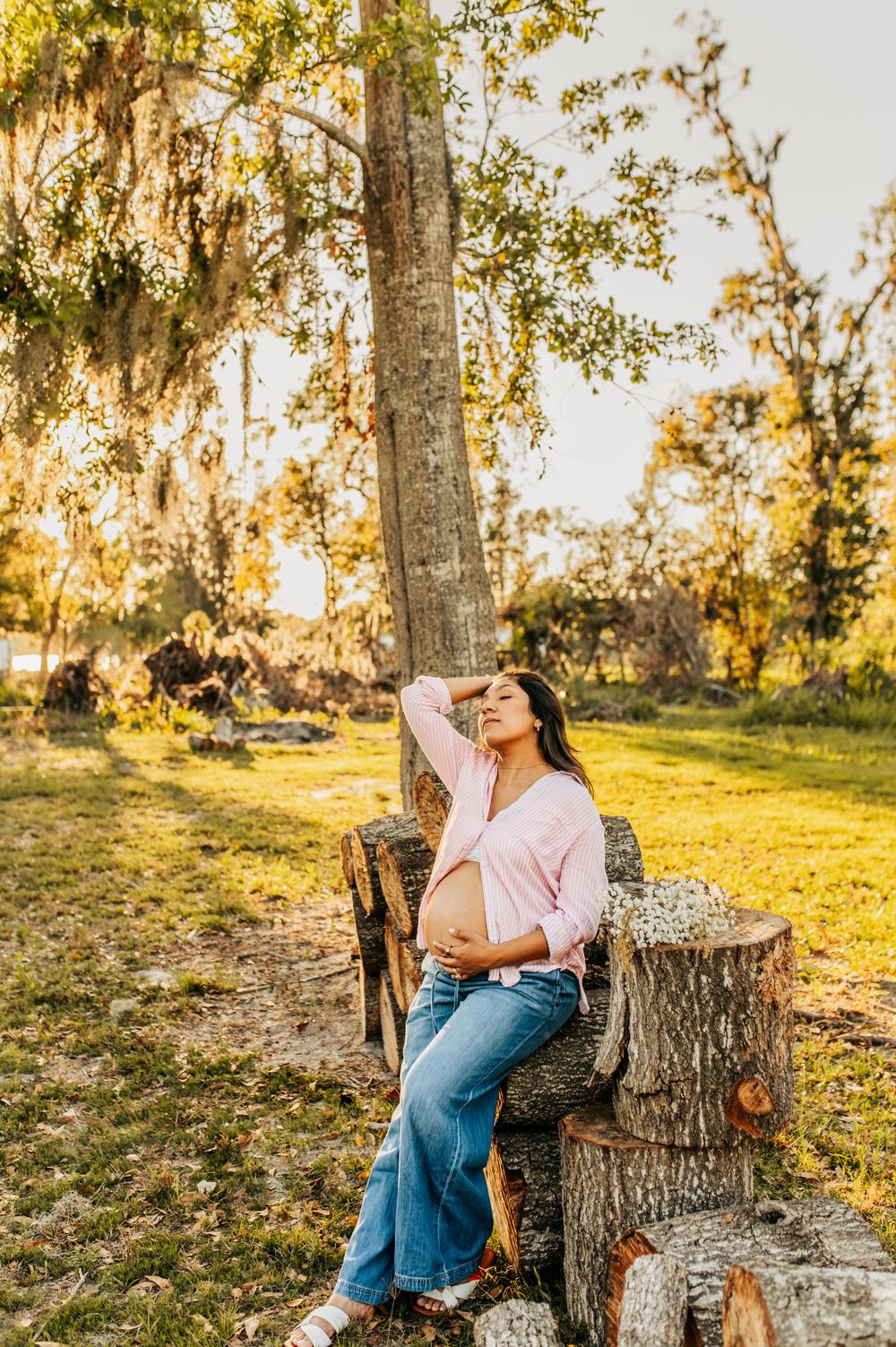 Couple sharing intimate moments on a tree stump during golden hour maternity photography session.
