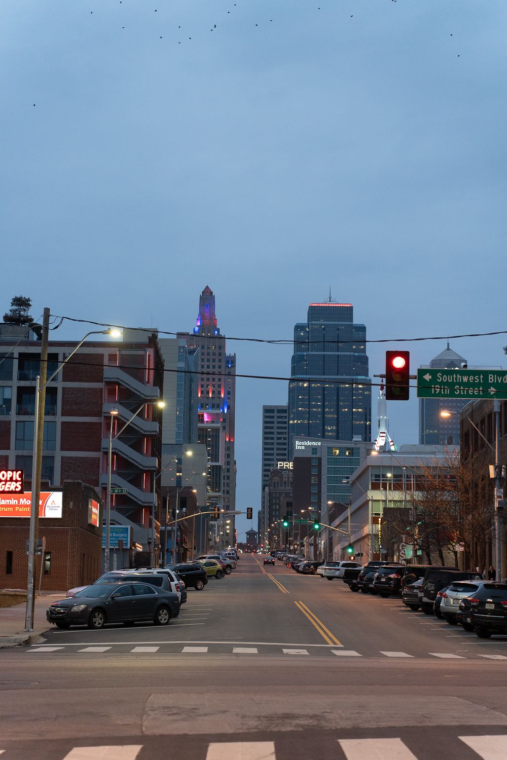 Downtown Kansas City street view at dusk with illuminated buildings and traffic lights.