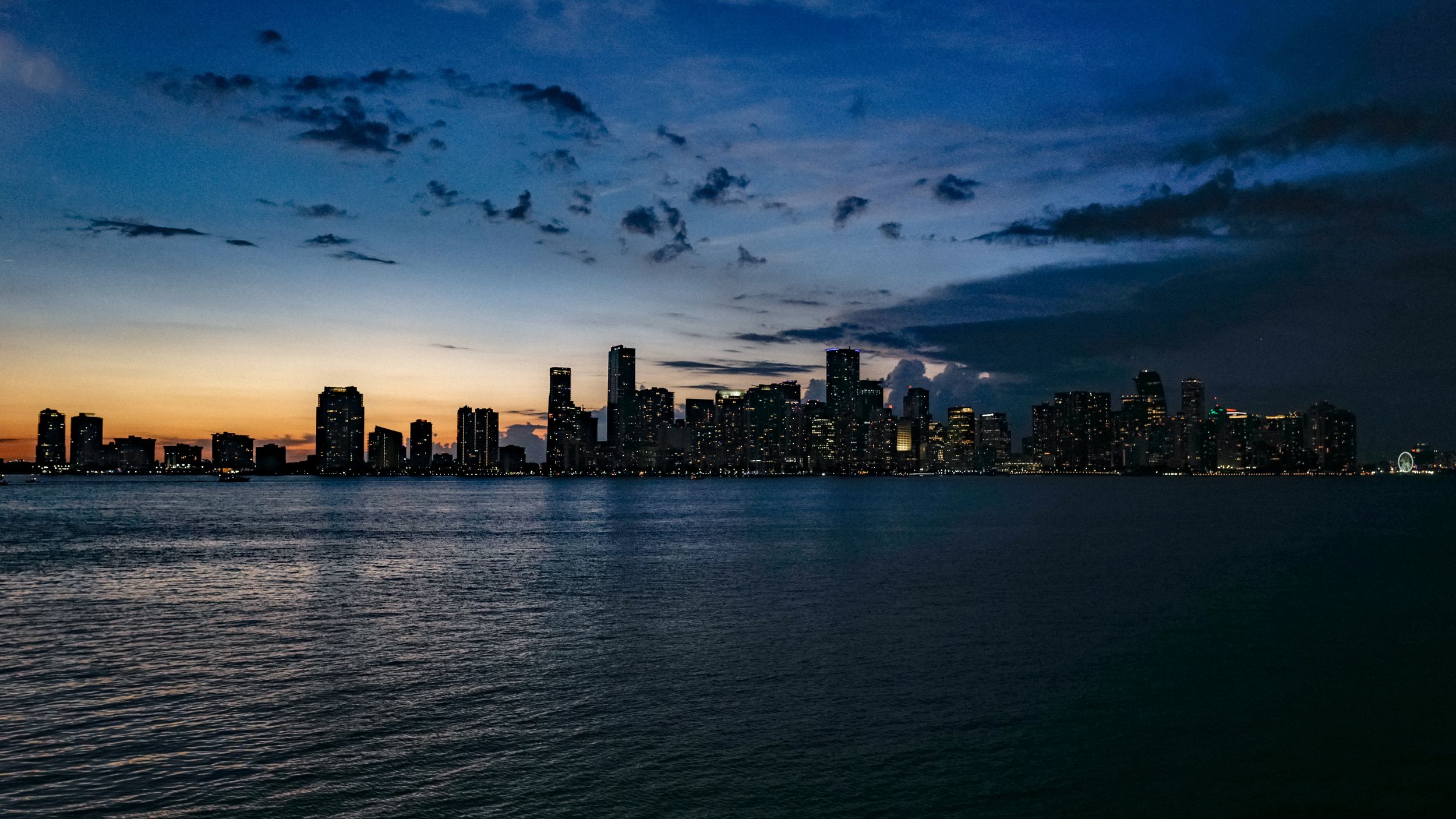 Miami skyline silhouetted against dramatic dusk sky over calm waters.
