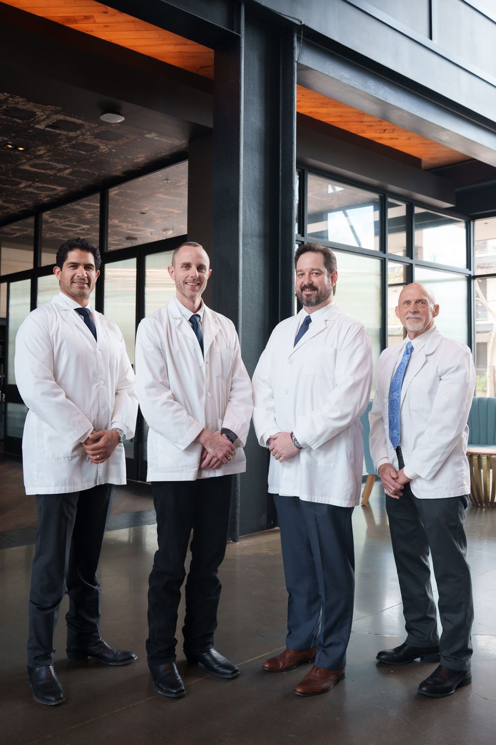 Four men wearing white lab coats stand together in a modern interior setting.
