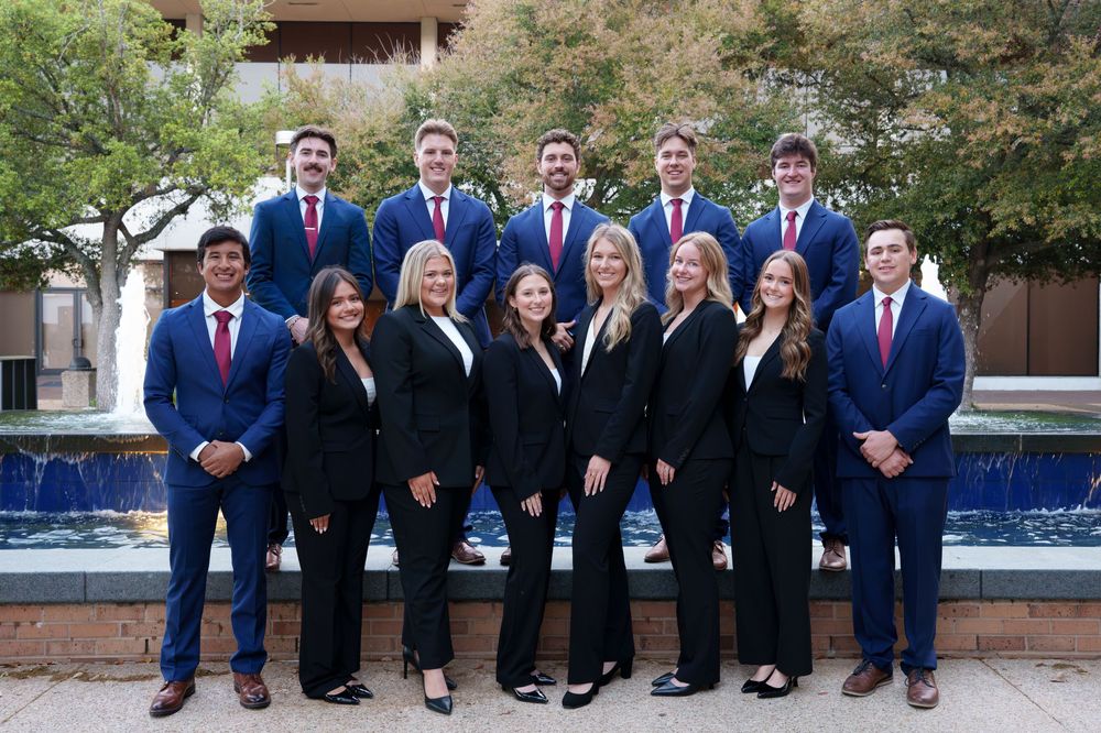 A group of people wearing suits and standing in front of a building with a water feature.