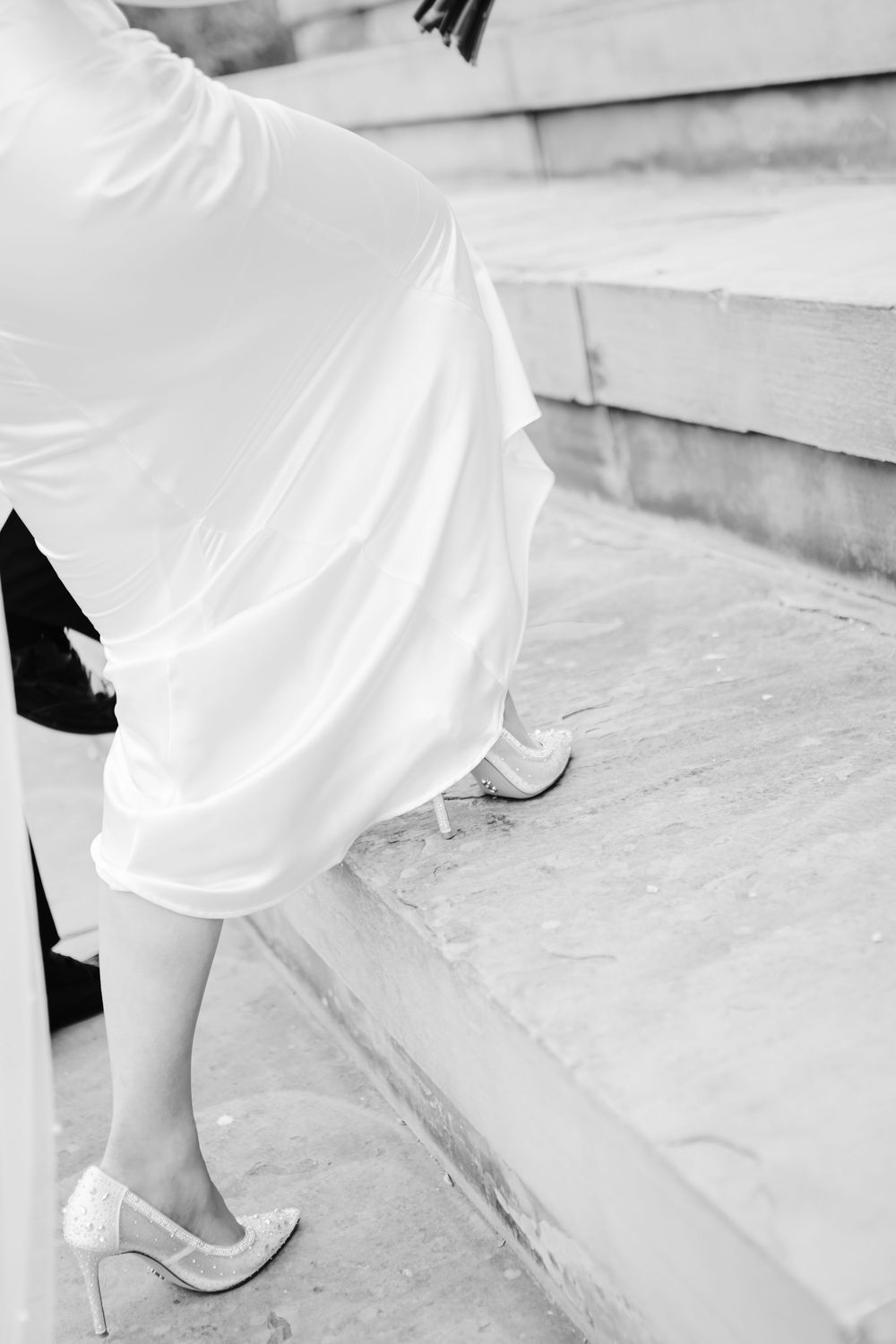 Bride in white wedding dress and heels ascending stone steps in black and white photo.