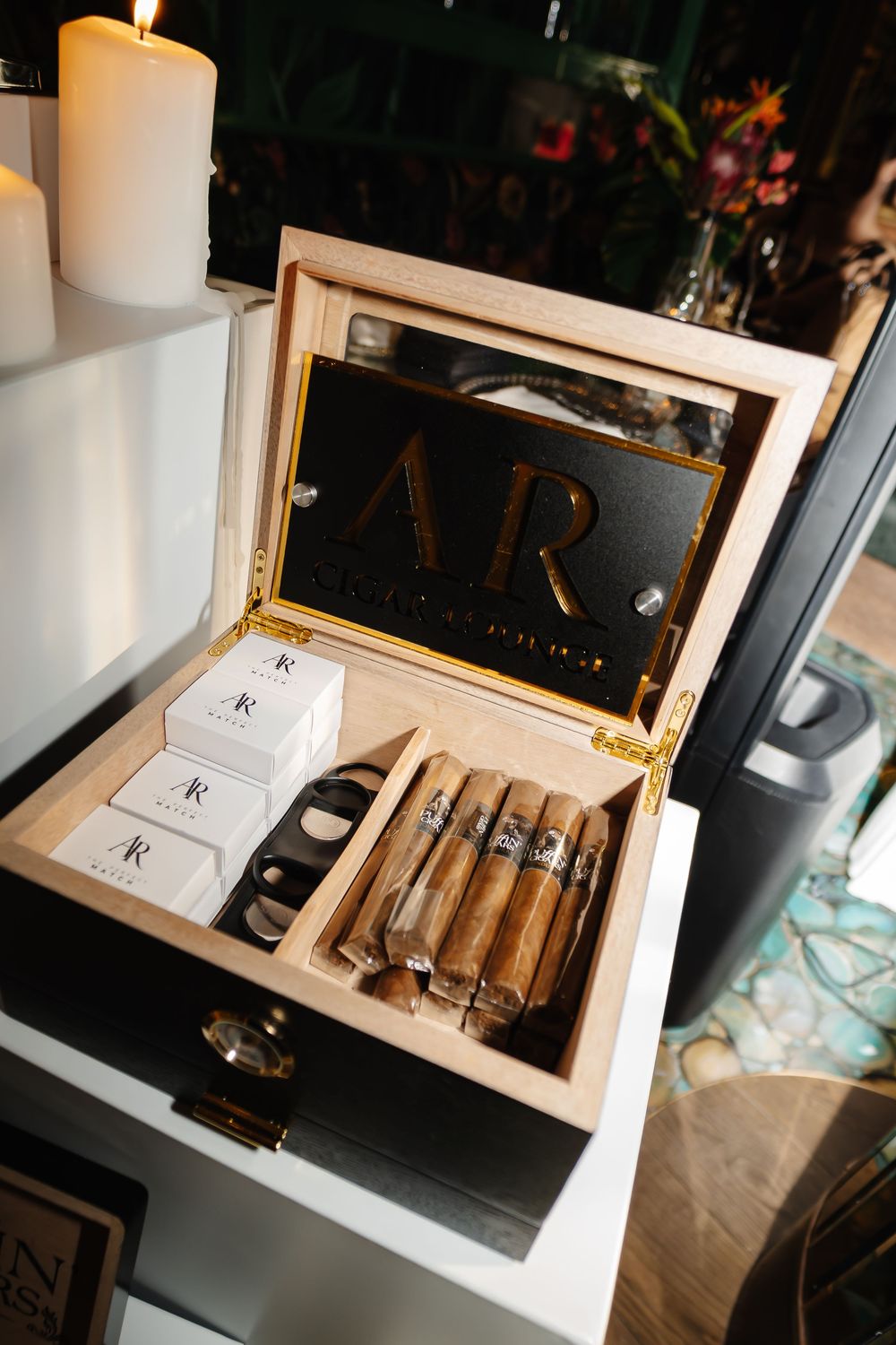 Personalized wooden humidor with AR monogram lid, cigars, and branded accessories displayed at an elegant event.