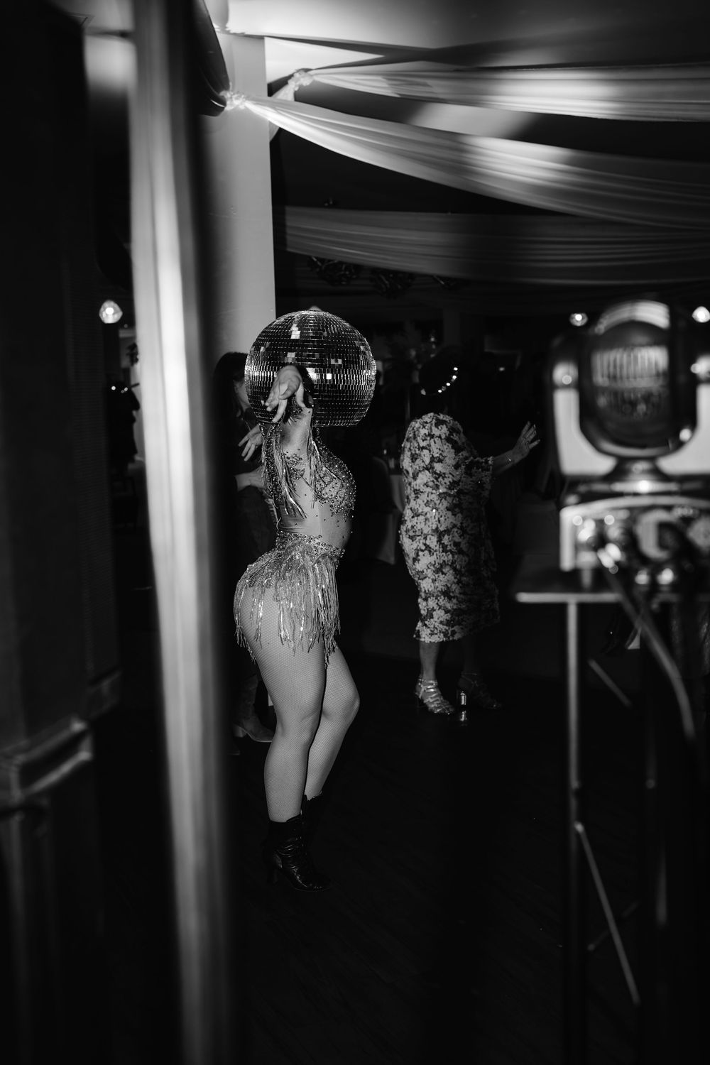 Black and white photo of a performer in a sequined outfit dancing under a disco ball at an elegant event.