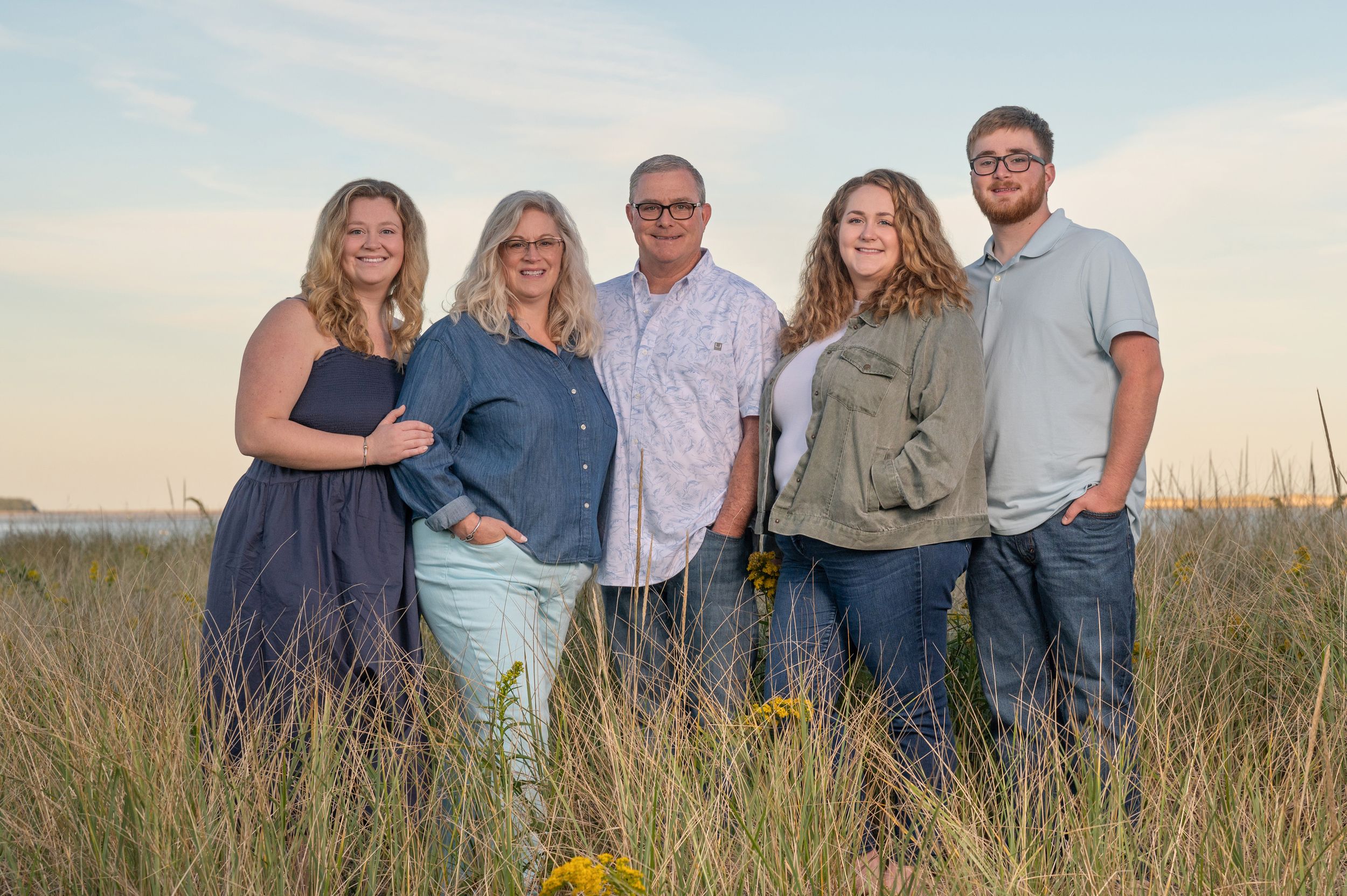 Group of people standing together in a grassy field during golden hour sunset.
