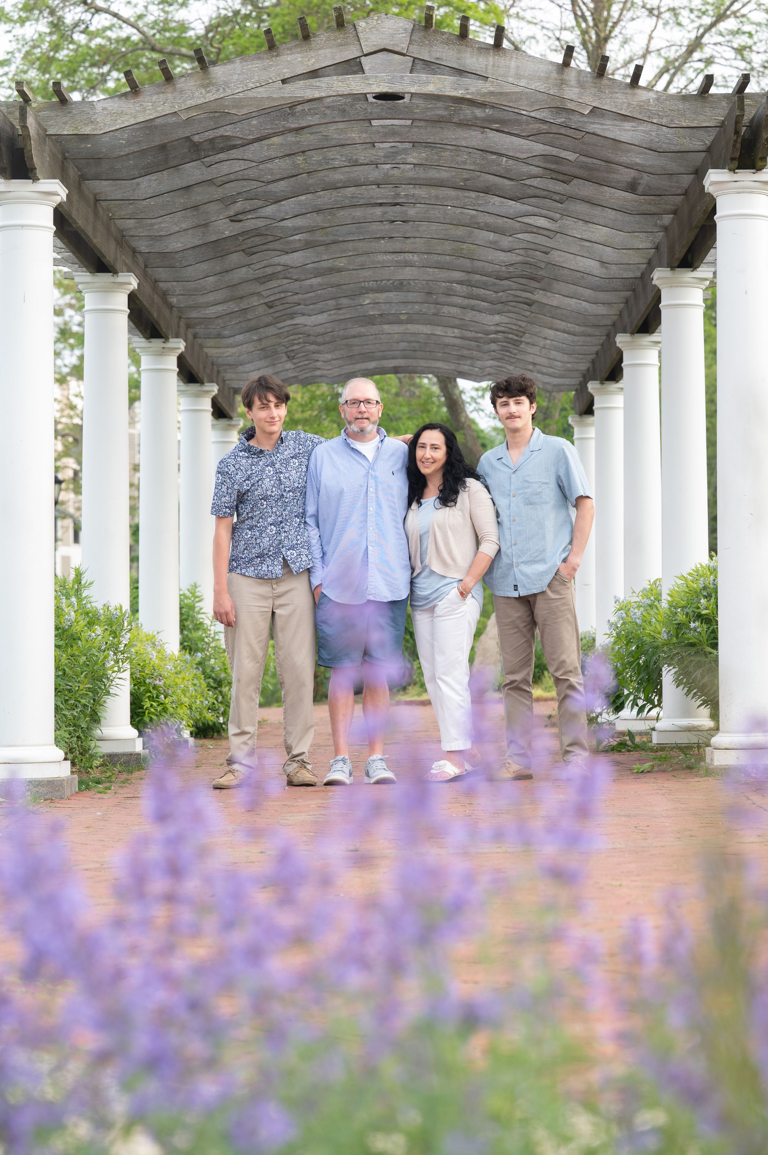 A group stands together under a white pergola with purple lavender flowers blooming in the foreground.