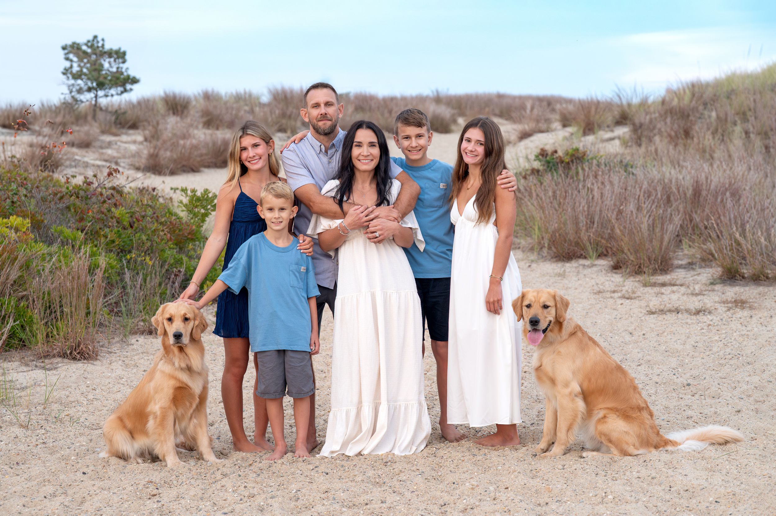 A golden retriever dog sitting on sandy beach during a family photo session at sunset.