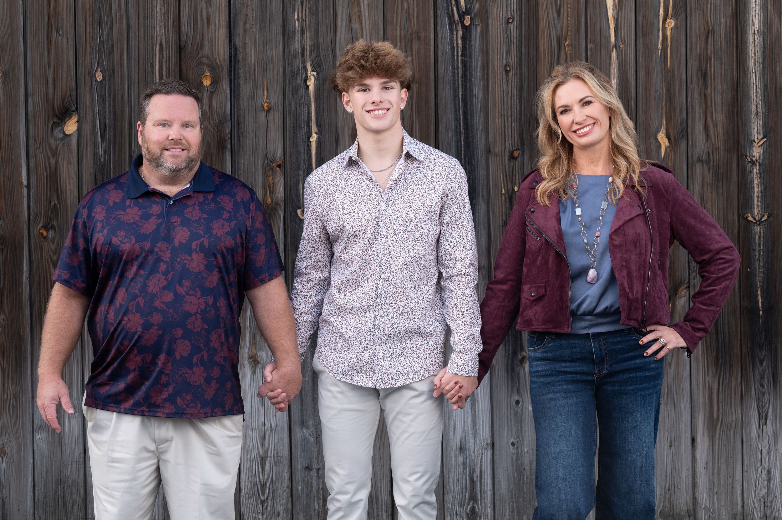 A group of people wearing casual clothing pose together against a rustic wooden fence background.
