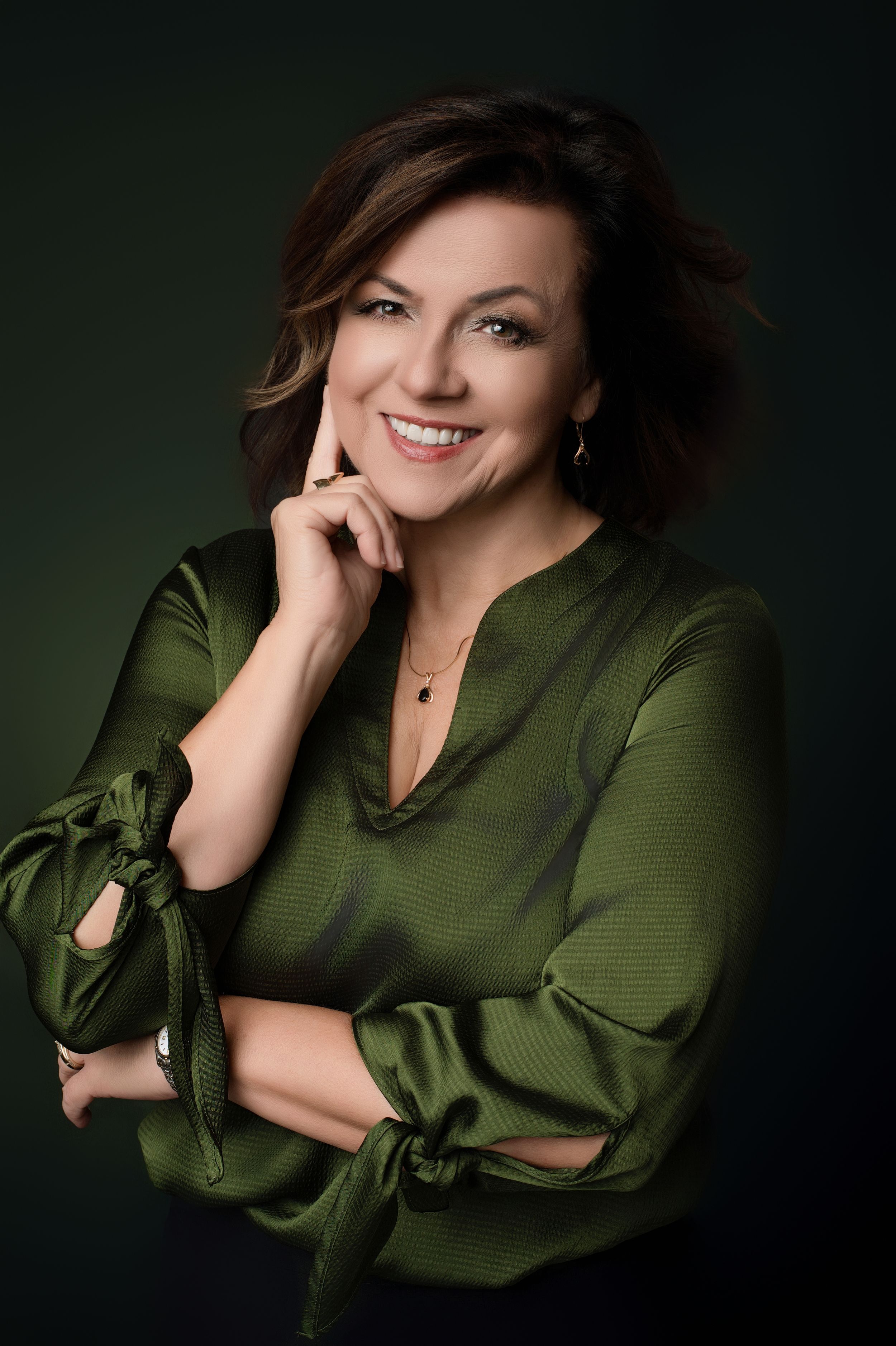 Elegant portrait with soft lighting showing a green silk top against a dark studio background.