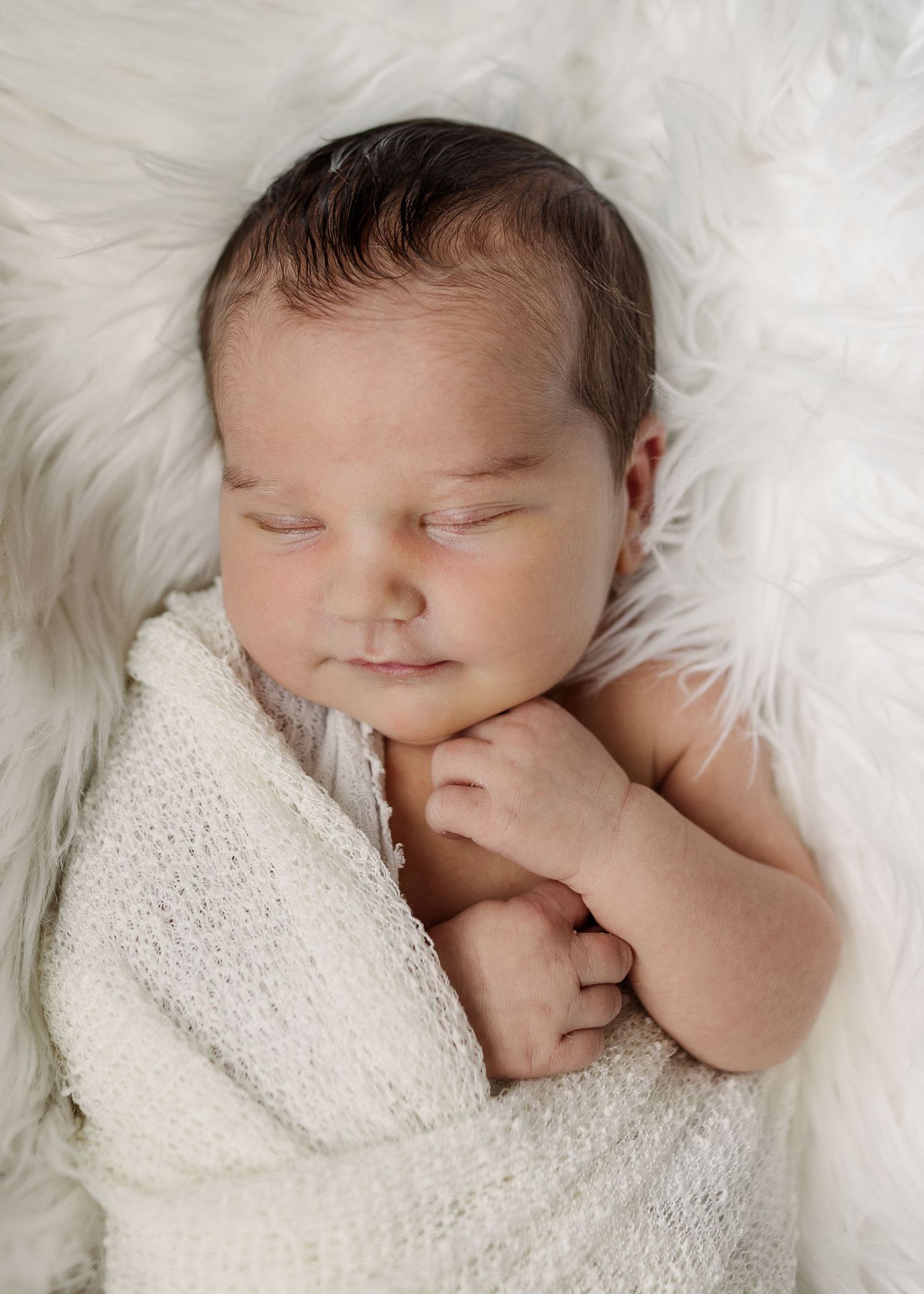 Peaceful sleeping newborn baby wrapped in white blanket on soft fur, by best San Antonio Photographer.