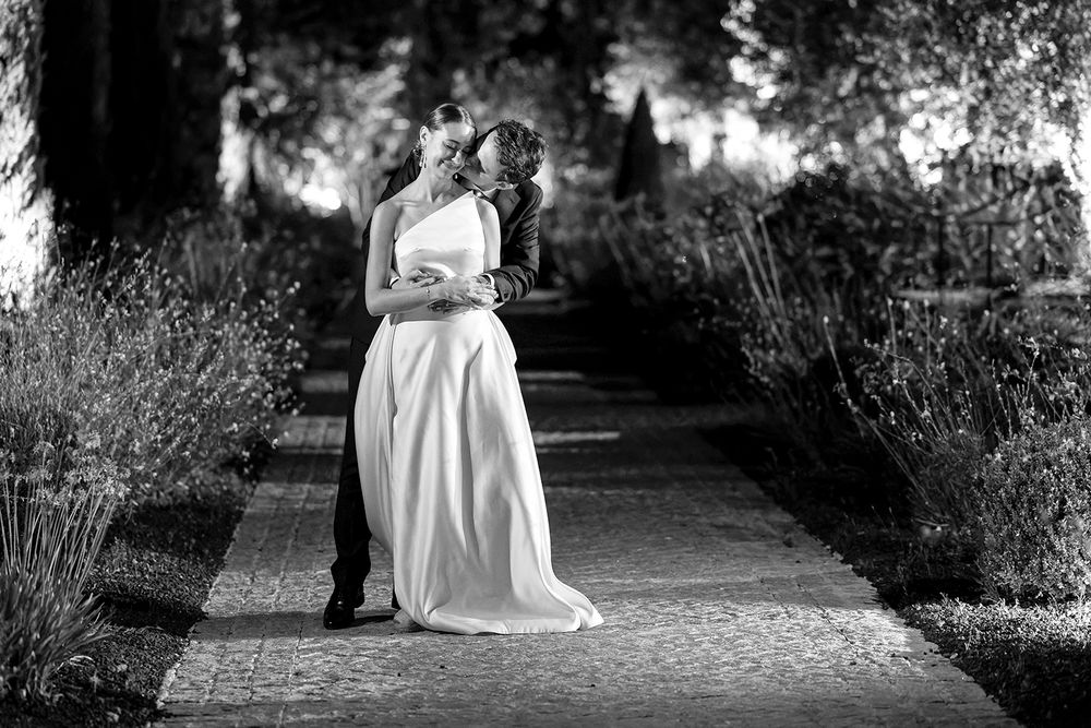 Artistic black and white photo of newlyweds on garden path surrounded by lavender.