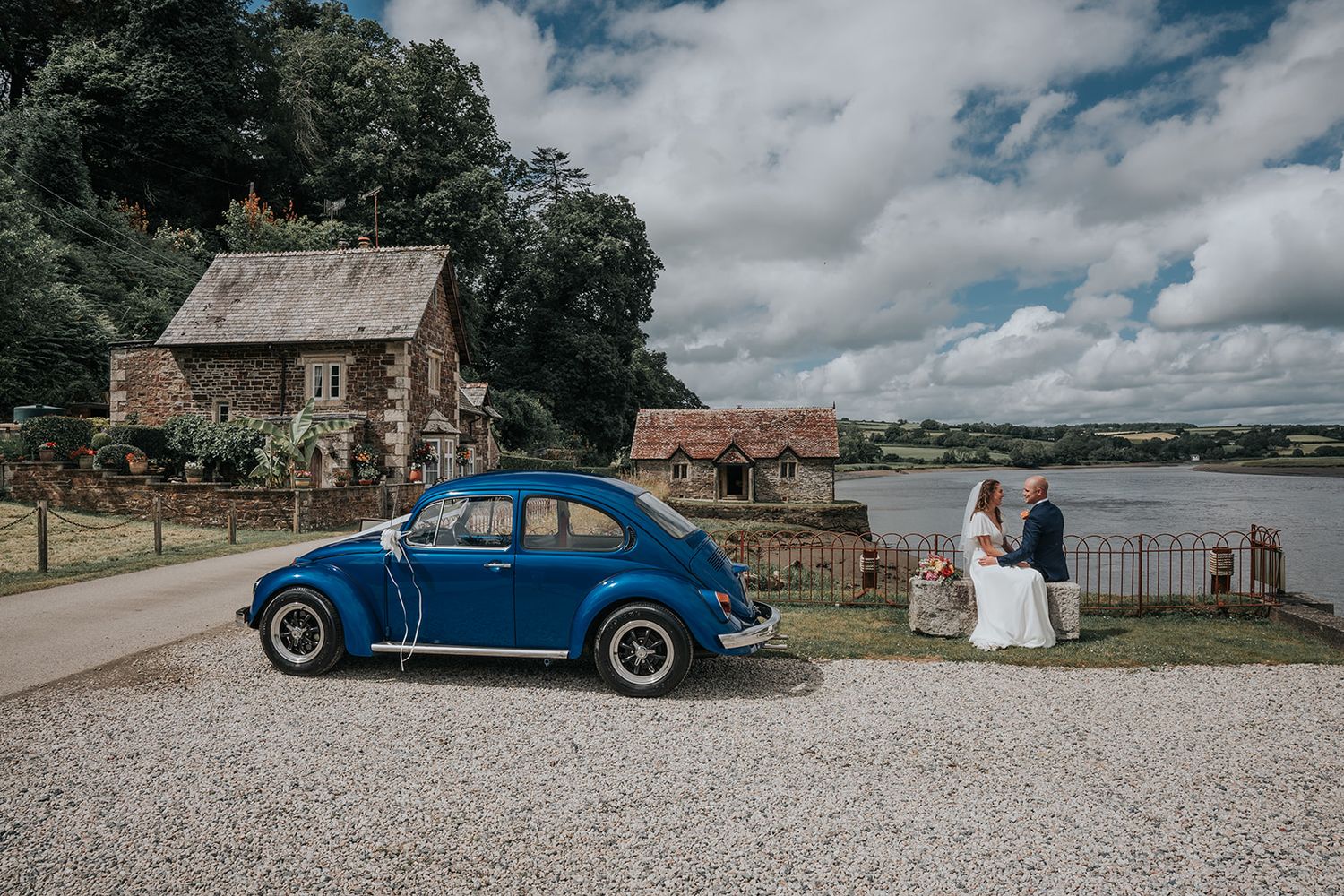 Wedding couple sat by the river infront of ceremony with wedding car and gorgeous views over cornwalls tamar river