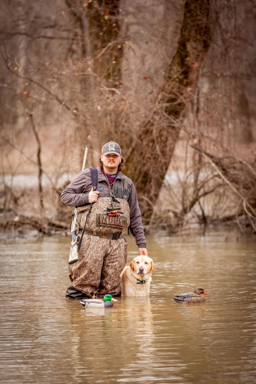 duck hunting senior boy in waders in water with gun, dog and decoy on cloudy day at Henry Gray Hurricane Lake WMA, Bald Knob, Arkansas