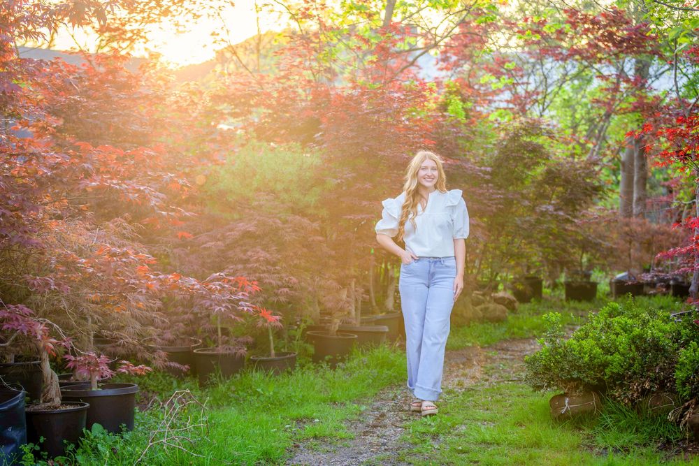senior girl in jeans white shirt and sandals in sunset light standing in a nursery garden in historic downtown Batesville, Arkansas