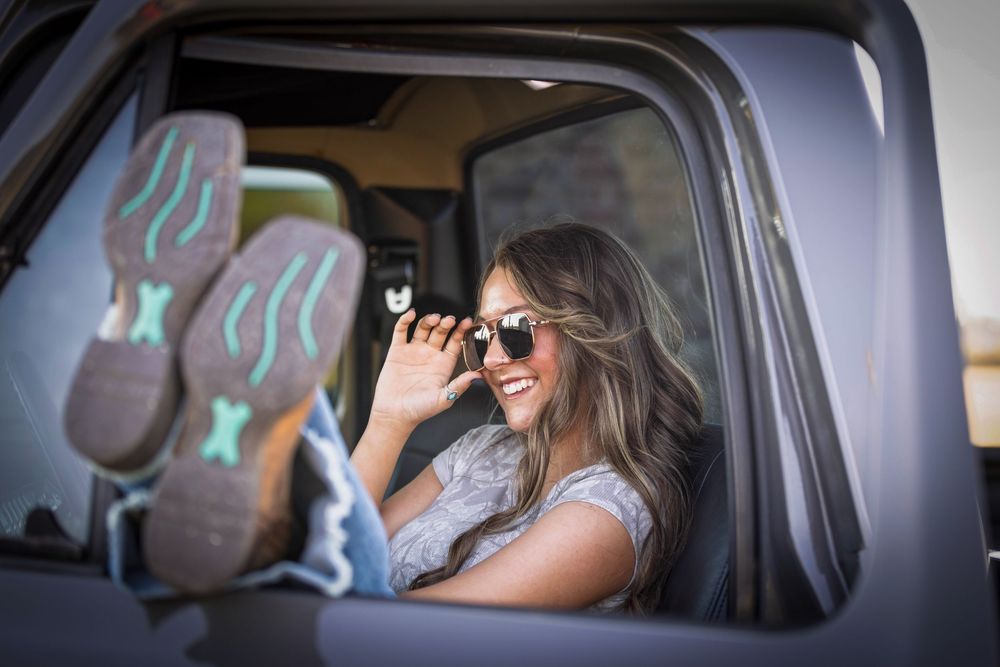senior girl in sunglasses sitting in classic gray truck with cowgirl boots out the window in a field outside Searcy, Arkansas
