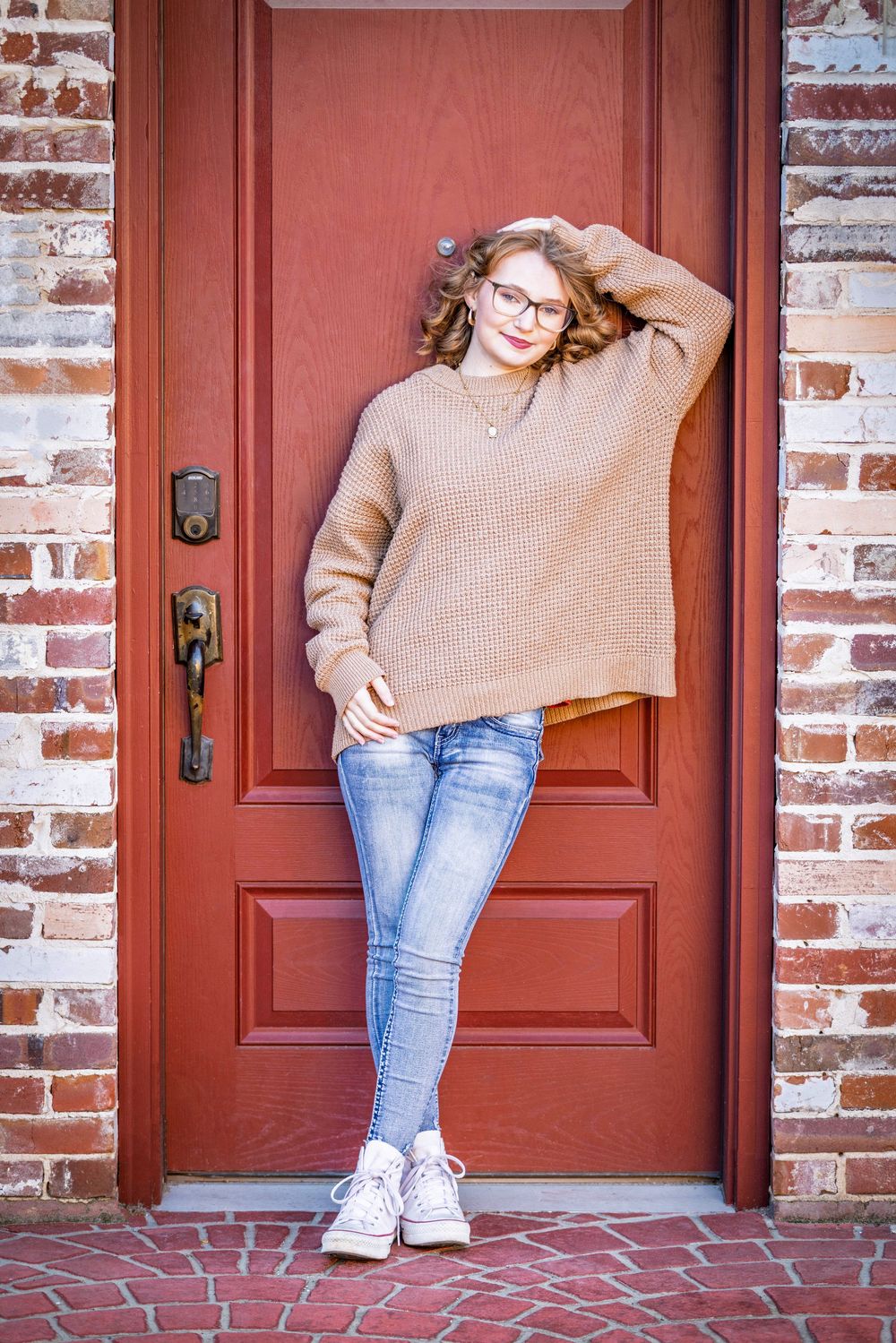 senior girl posing in the doorway of a red door surrounded by red and white bricks in evening shade in downtown Batesville, Arkansas