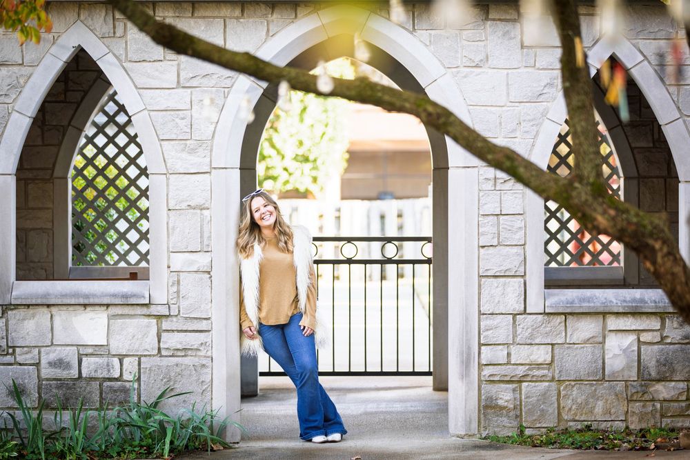 blonde senior girl in fuzzy vest leaning in an ornate outside chapel doorway in late evening shaded light in downtown Batesville, Arkansas
