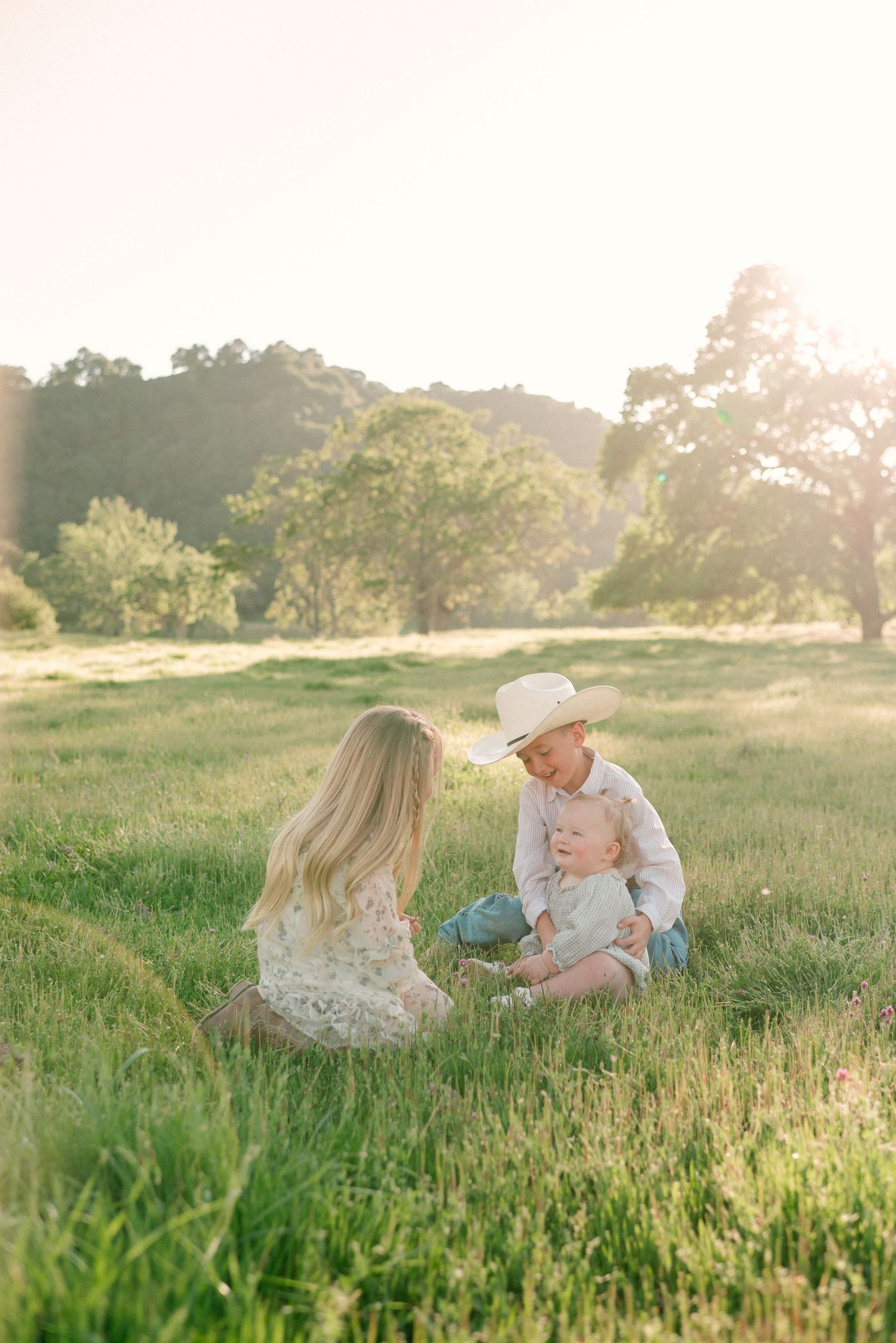 Family in coordinated neutral outfits poses together in golden field at sunset.