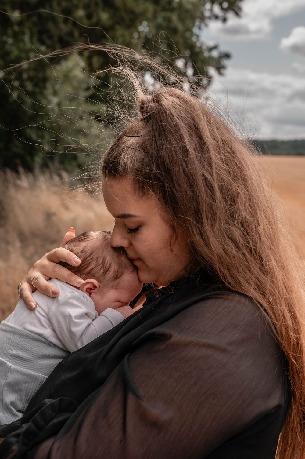 Two people sharing an intimate embrace outdoors with a field and cloudy sky in the background.