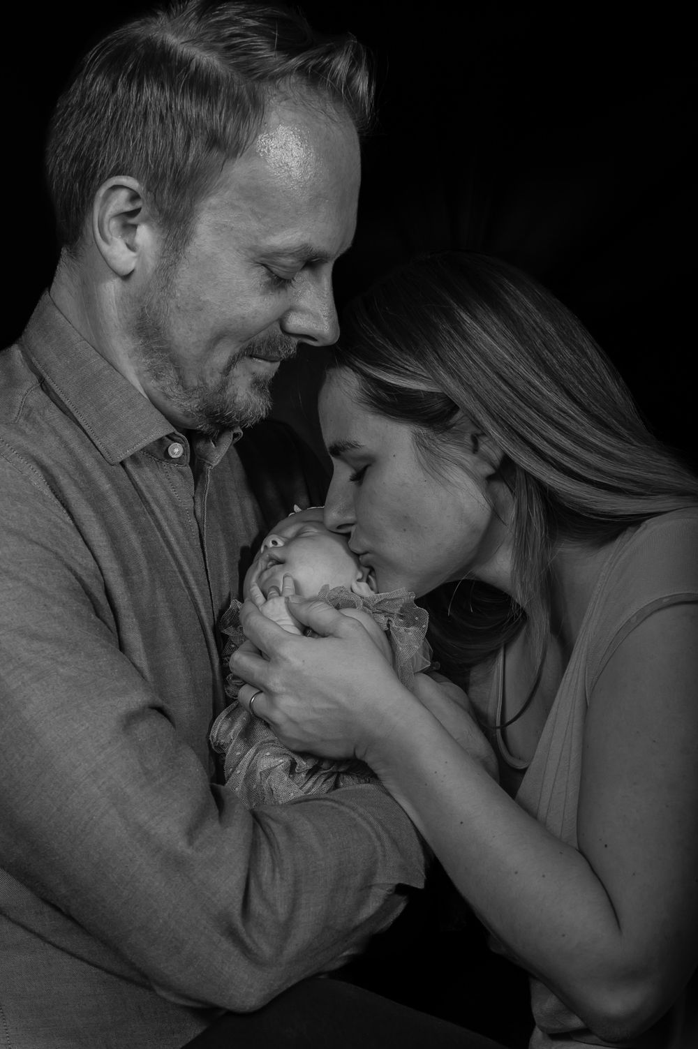 A tender black and white photo sequence shows a couple sharing an intimate moment with their newborn baby.