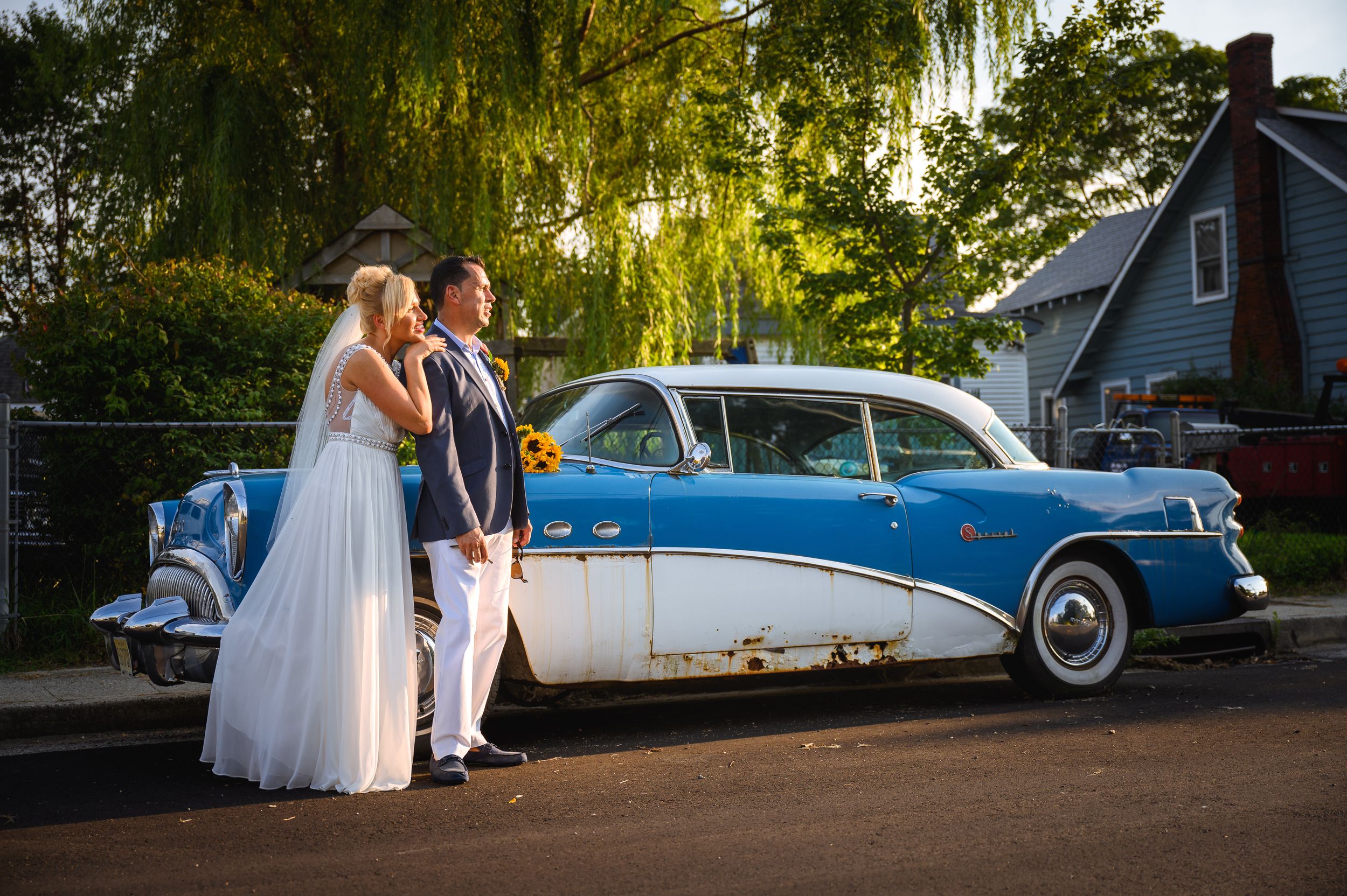 Couple poses with vintage blue and white classic car at wedding.