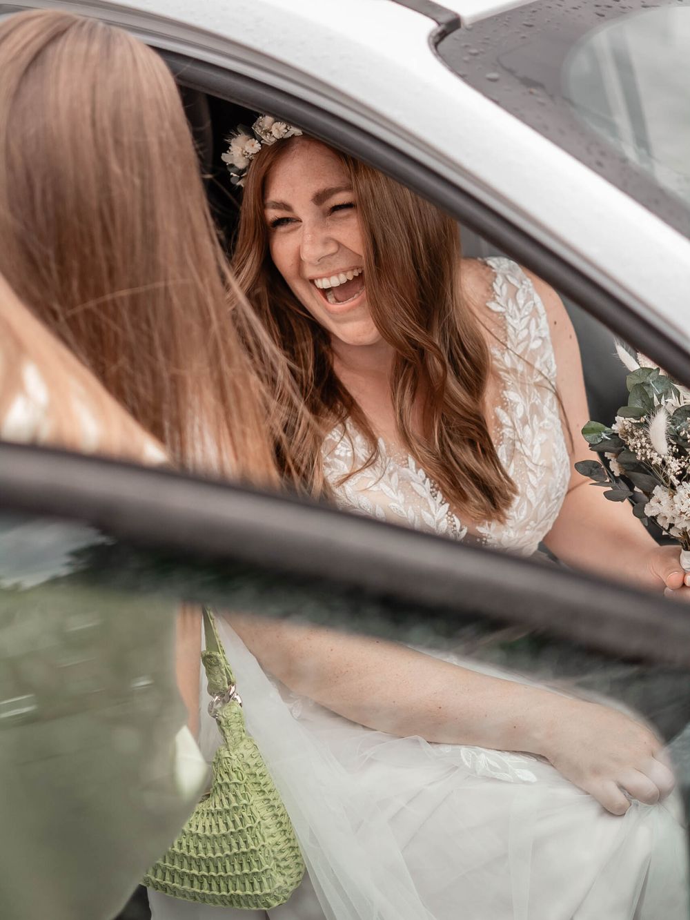 Happy person in a wedding dress shown through a car window holding a delicate bouquet of flowers.
