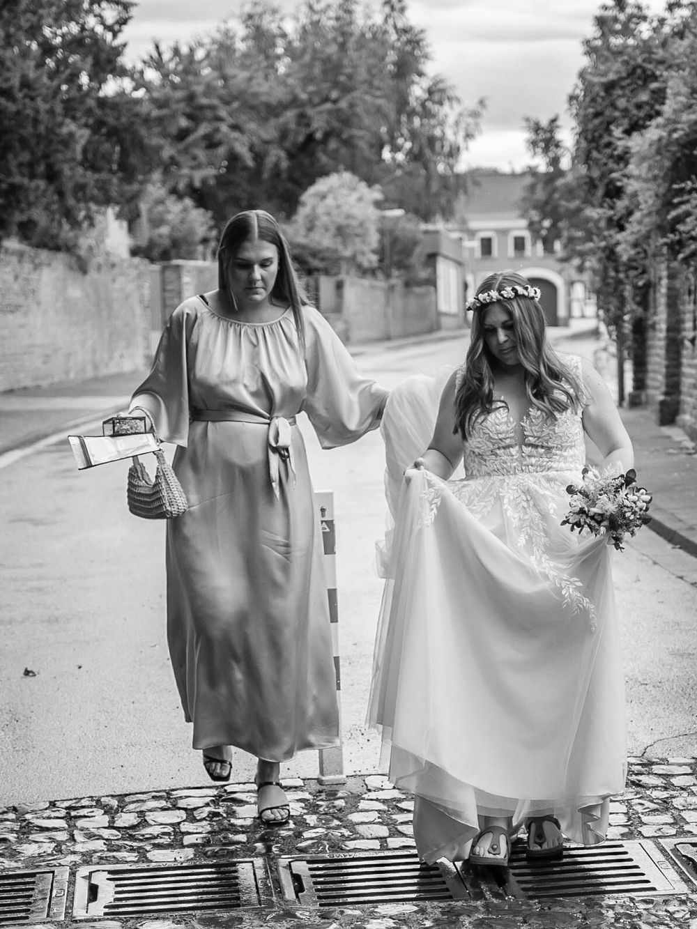 Four similar black and white photographs showing two people walking together on a path holding hands in flowing dresses.