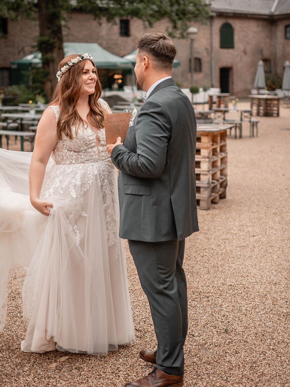 A couple shares an intimate moment in front of a rustic brick building, with the bride wearing a flowing tulle gown.
