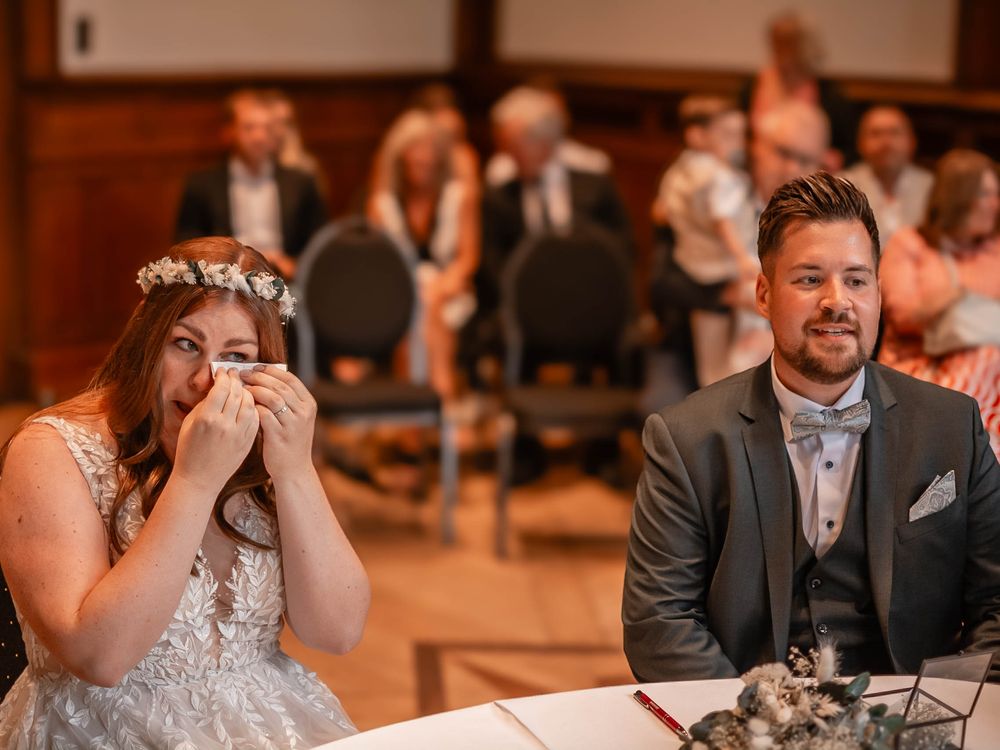 Bride and groom share emotional moment while sitting at decorated wedding table in warm-lit reception venue.