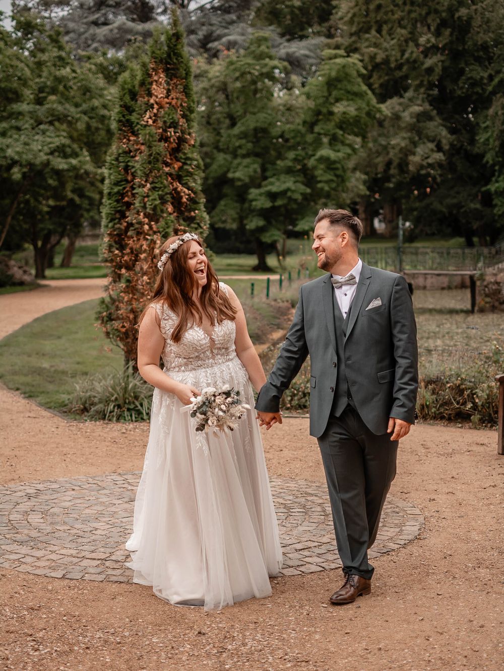A couple takes a romantic stroll together along a garden path as autumn leaves fall around them in natural lighting.