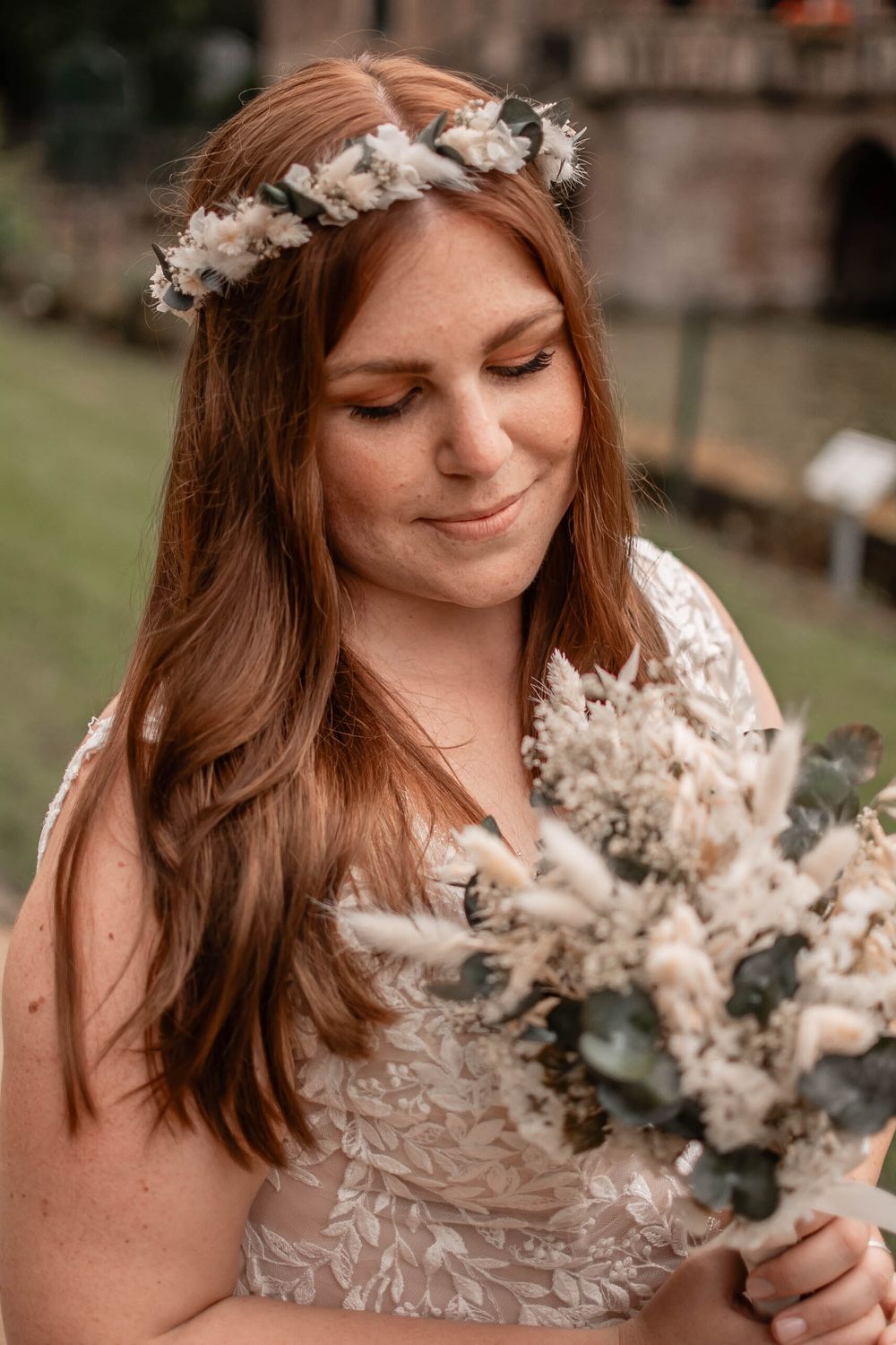 A bride in a white ruffled dress holds a delicate dried floral bouquet in soft natural lighting.