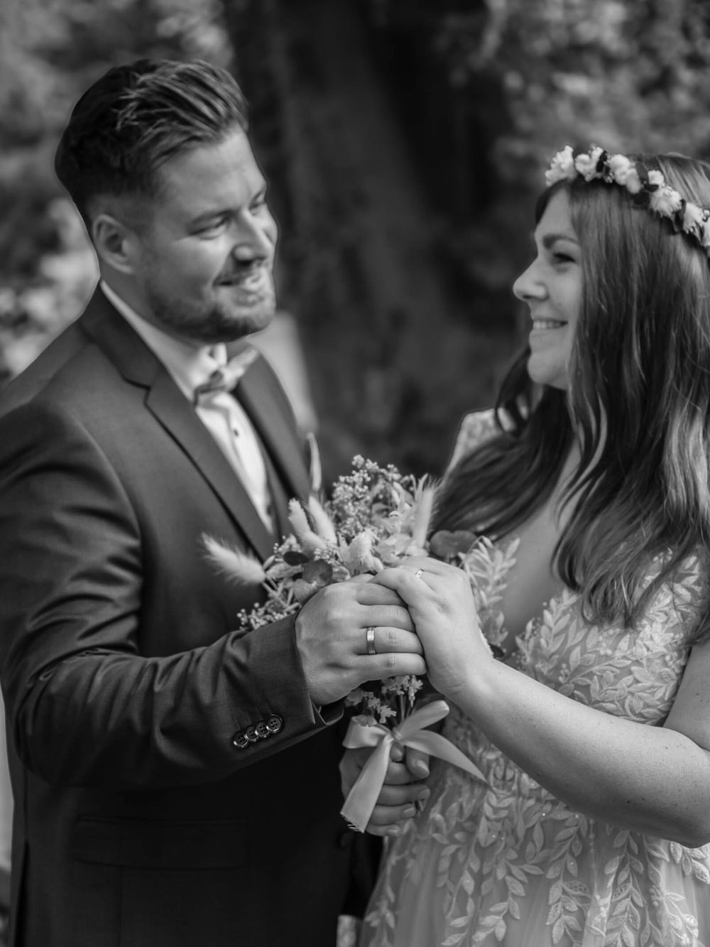 A romantic black and white wedding portrait of a couple sharing a tender moment with flowers in their hands.