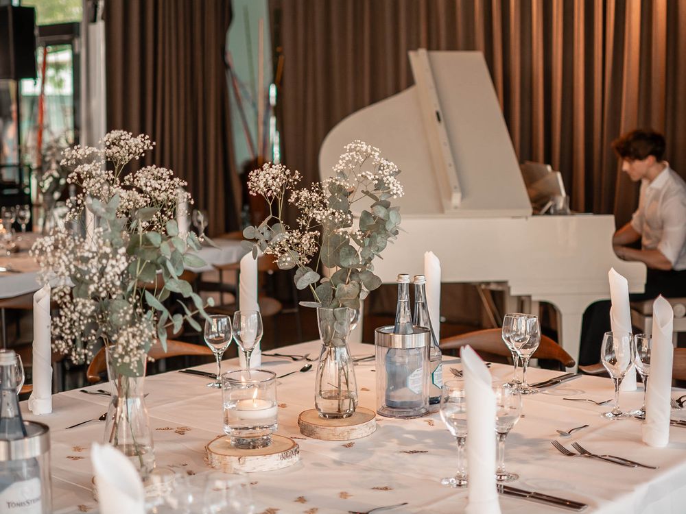 Elegant white floral centerpieces with baby's breath and candlelight decorate reception tables at an indoor wedding venue.