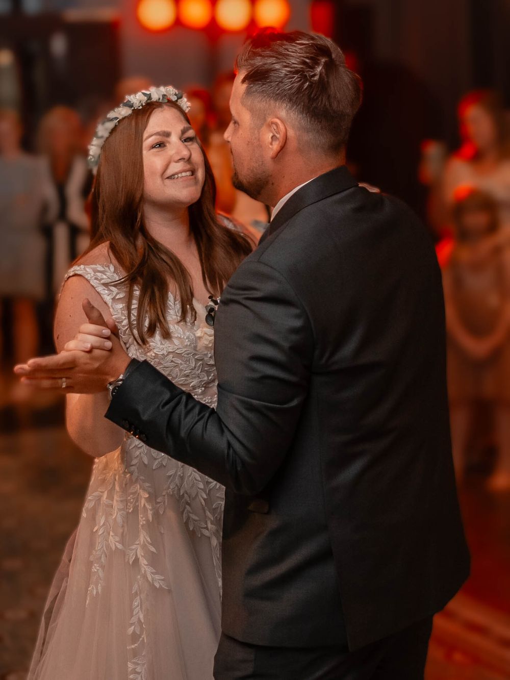 A couple shares a romantic dance moment at their wedding reception under warm ambient lighting.
