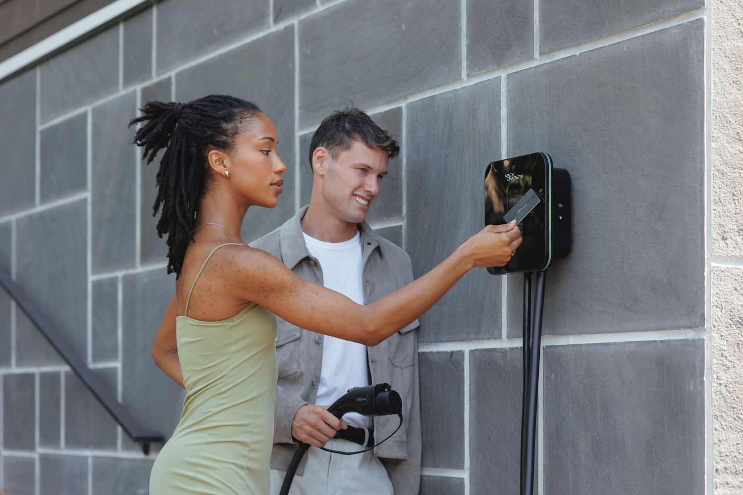Woman in green dress and man in suit pose together against a gray wall.