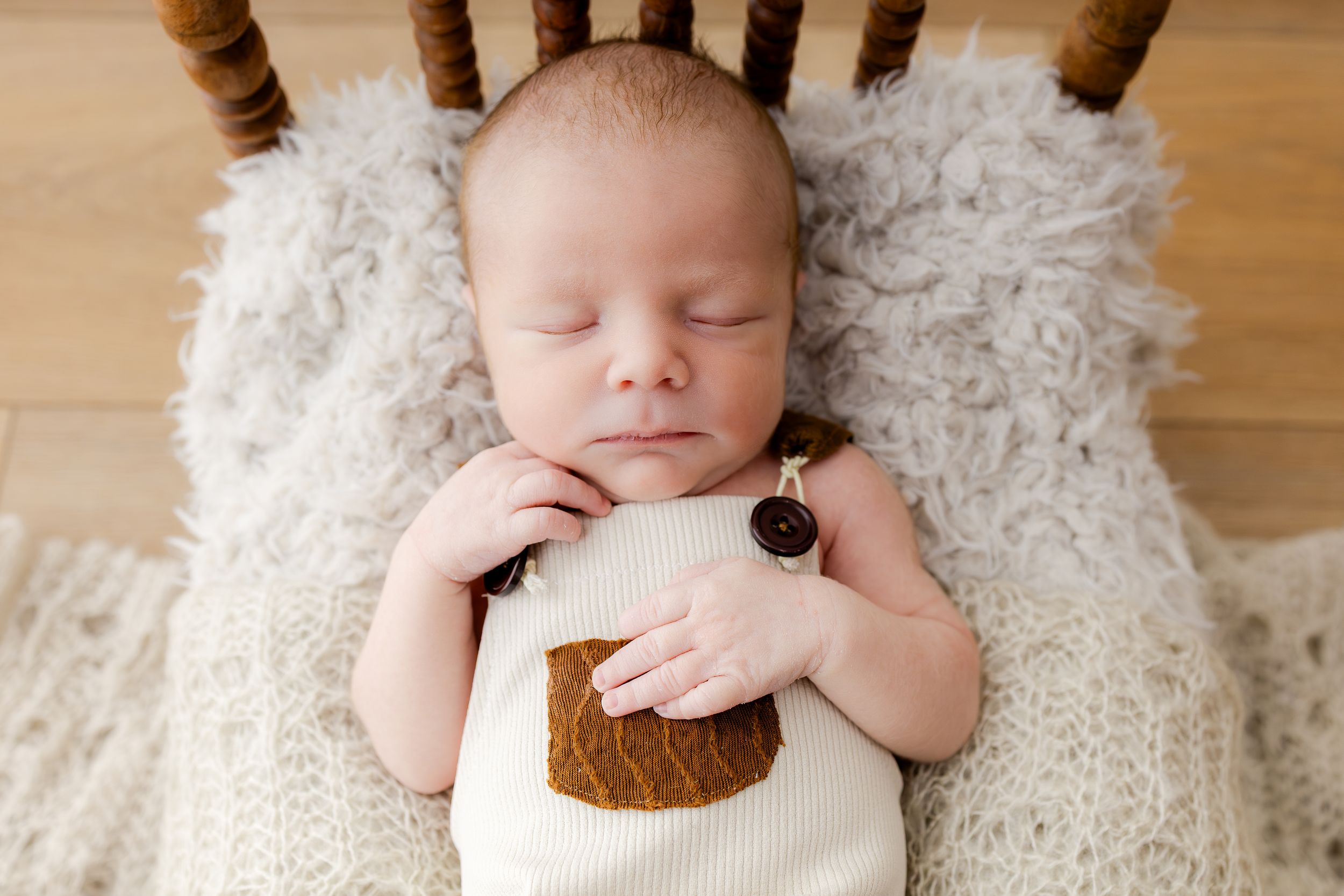 Peaceful newborn baby sleeping in a wooden chair on a knit blanket, wearing a cute bear outfit.