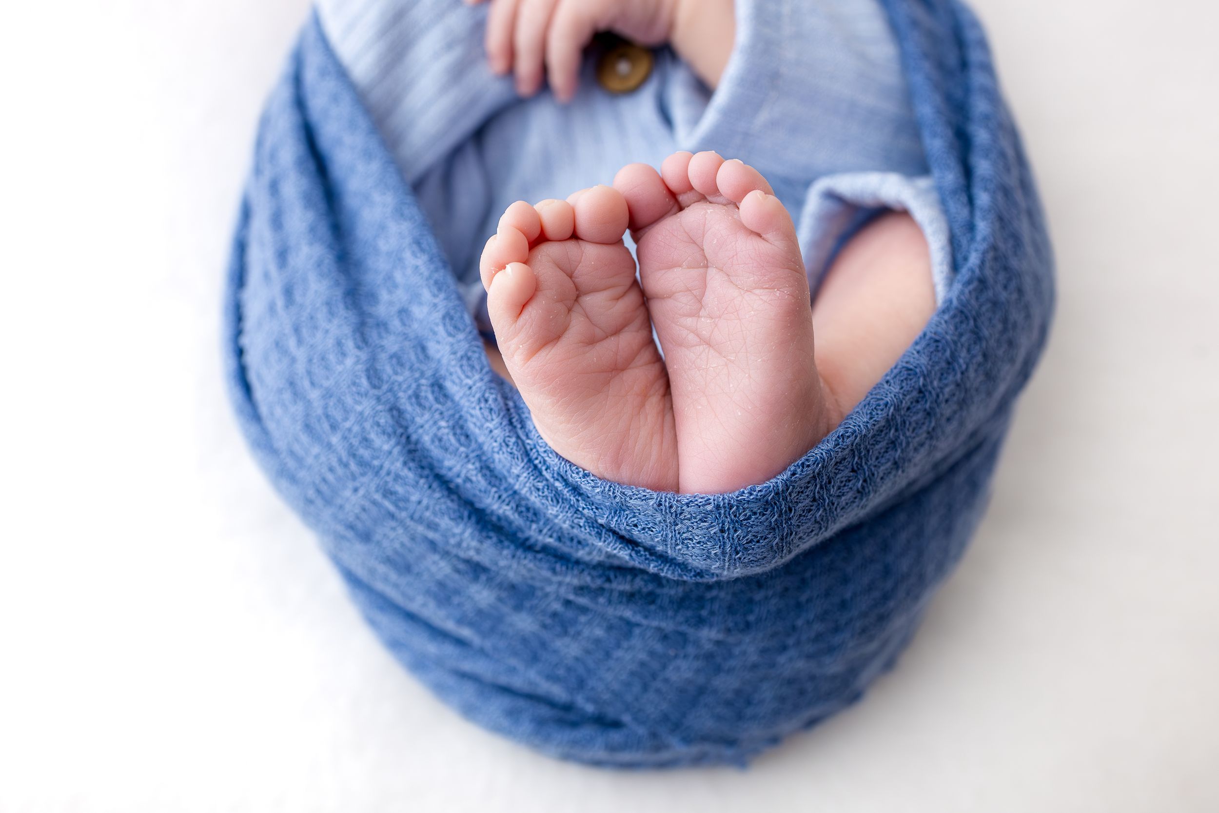 Newborn baby feet peeking out of a soft blue swaddle wrap on a white background.