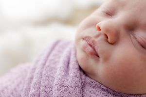 Close-up macro photography of a sleeping baby wearing soft pink knit clothing.
