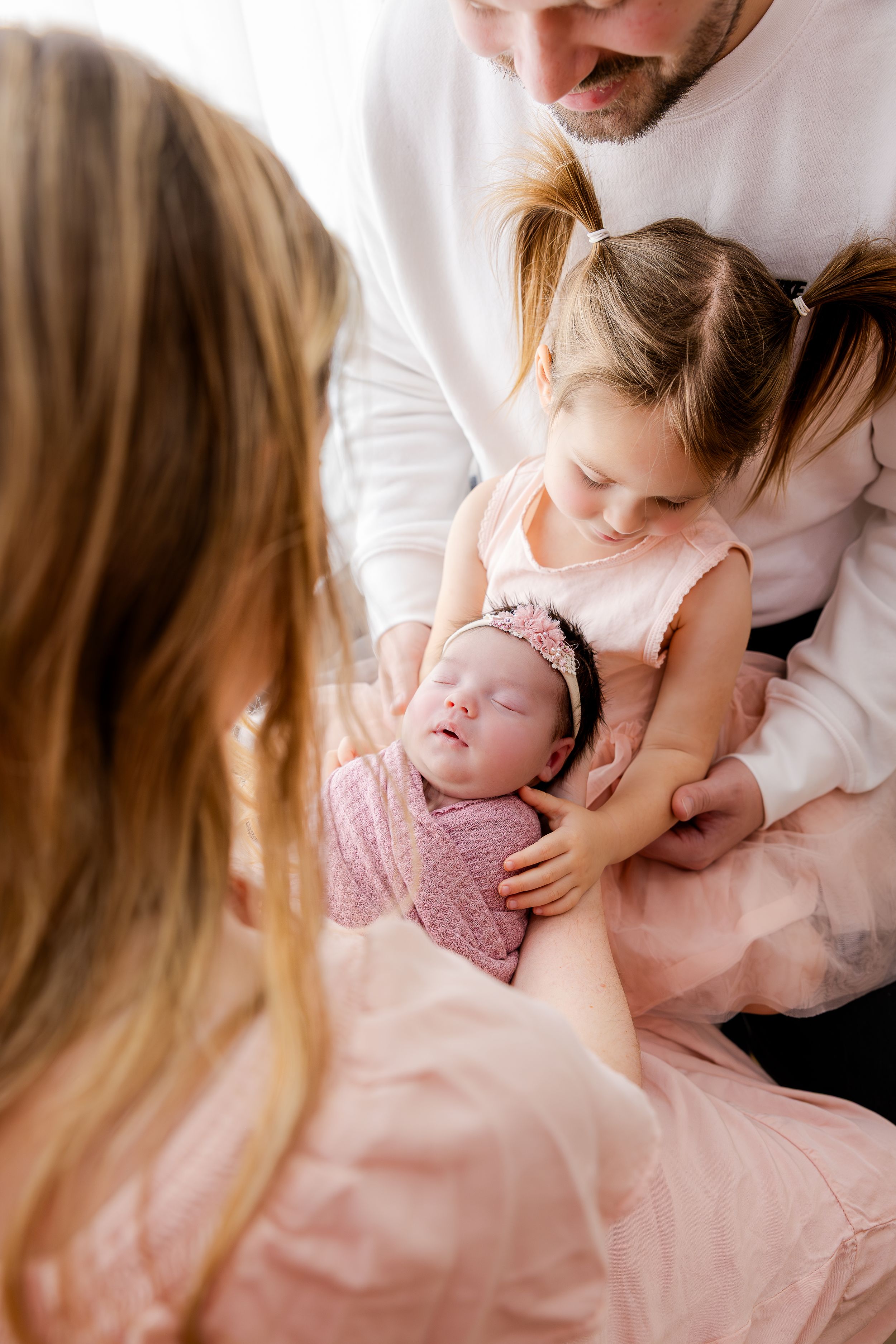A series of intimate family portraits showing tender moments between parents and their newborn baby in soft pink tones.