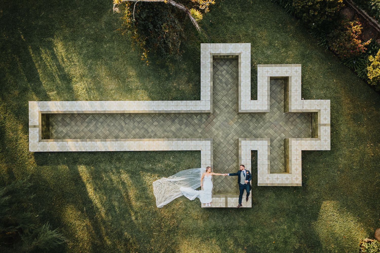 Toma aérea con dron de novios sobre estructura en forma de cruz / Aerial drone shot of bride and groom on cross-shaped structure.