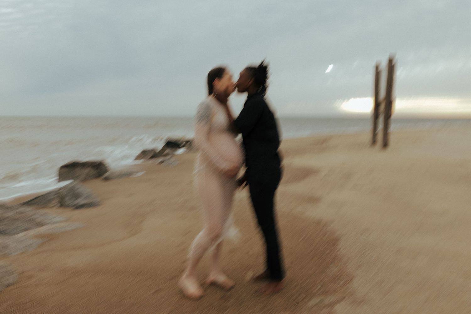 Two silhouetted figures dance on a misty beach with waves and wooden posts in the background.