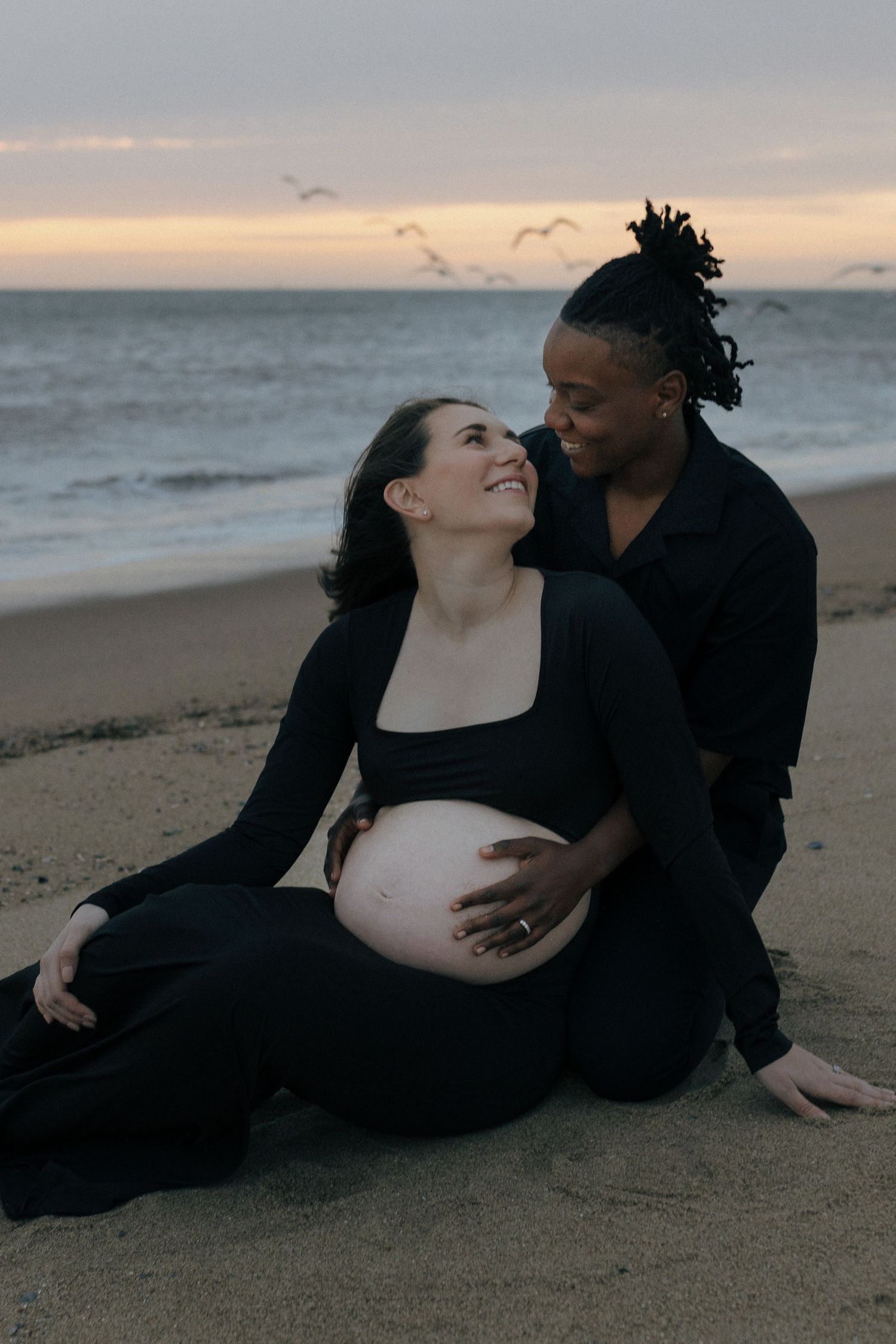 A tender maternity moment captured at sunset on the beach as a couple embraces on the sand.
