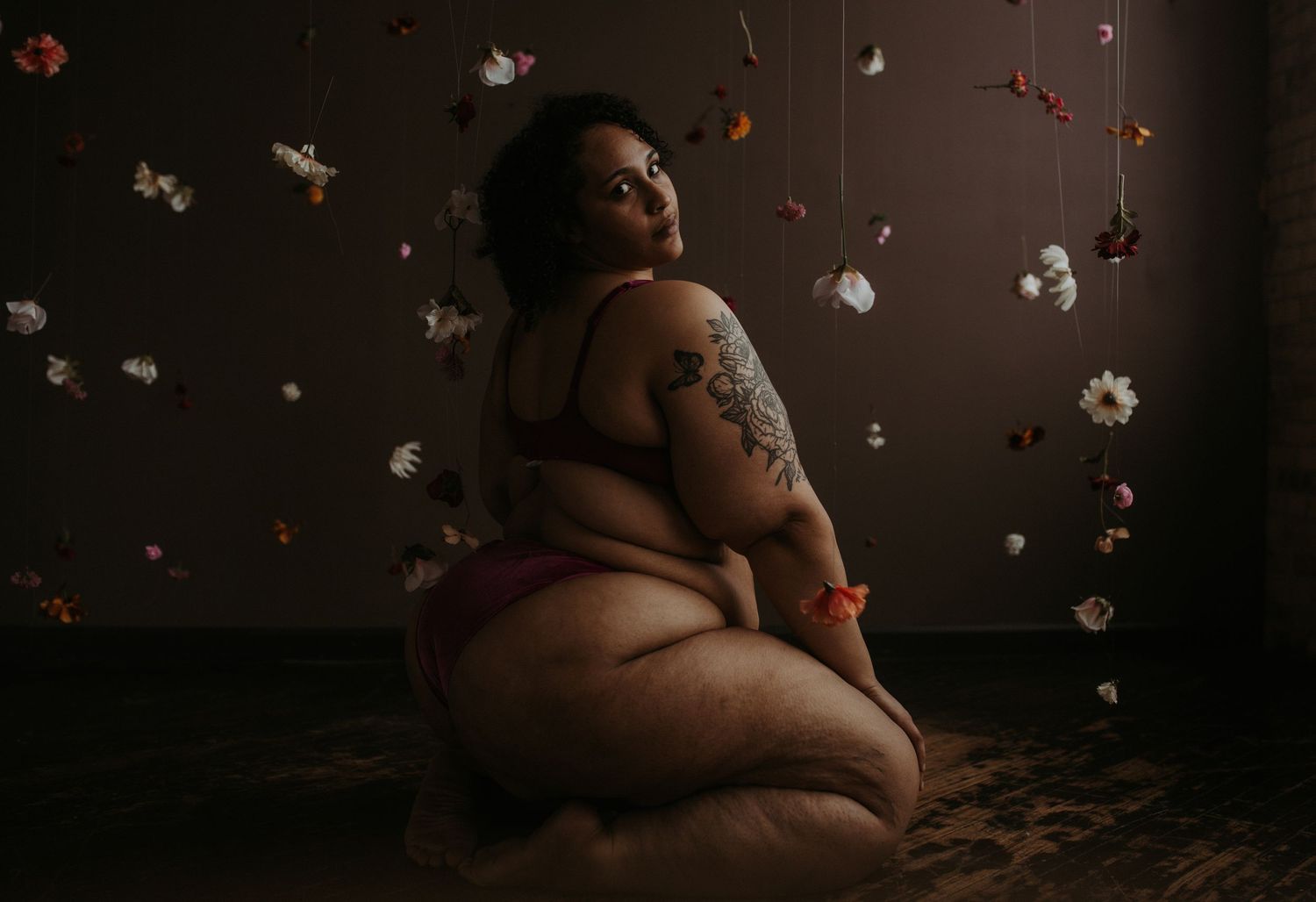 A person in black lingerie reclines on a floral patterned couch in moody lighting.