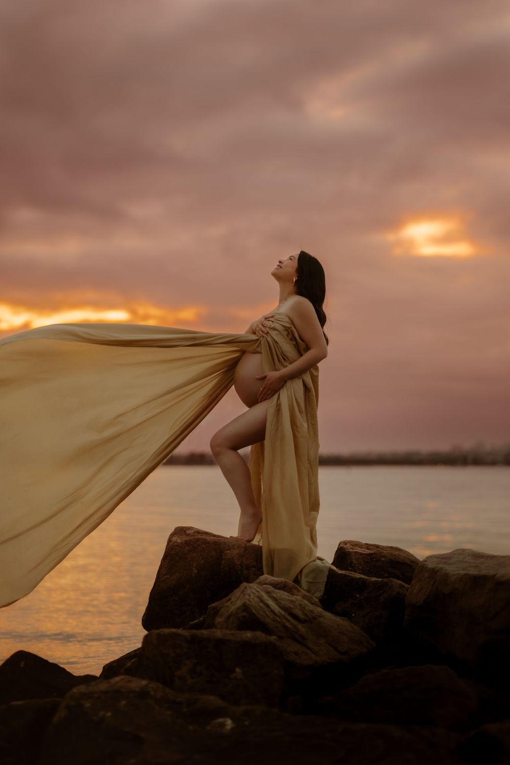 Woman in white dress lying on beach shore during golden sunset.