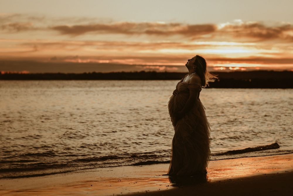 Woman in white dress lying on beach shore during golden sunset.